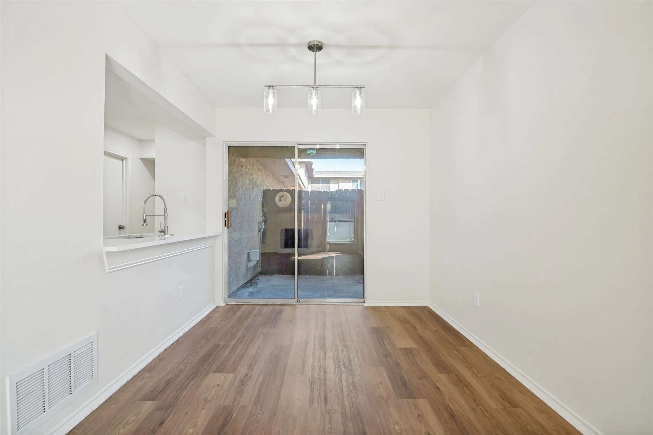 Bright interior space featuring wood-finish flooring, a contemporary three-light pendant fixture, and a large sliding glass door opening to an outdoor patio