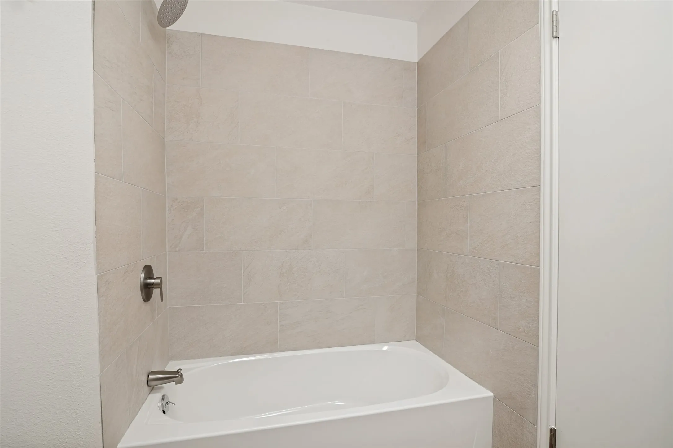 Built-in bathtub featuring light-toned tile surround, brushed nickel fixtures, and a ceiling-mounted rainfall showerhead