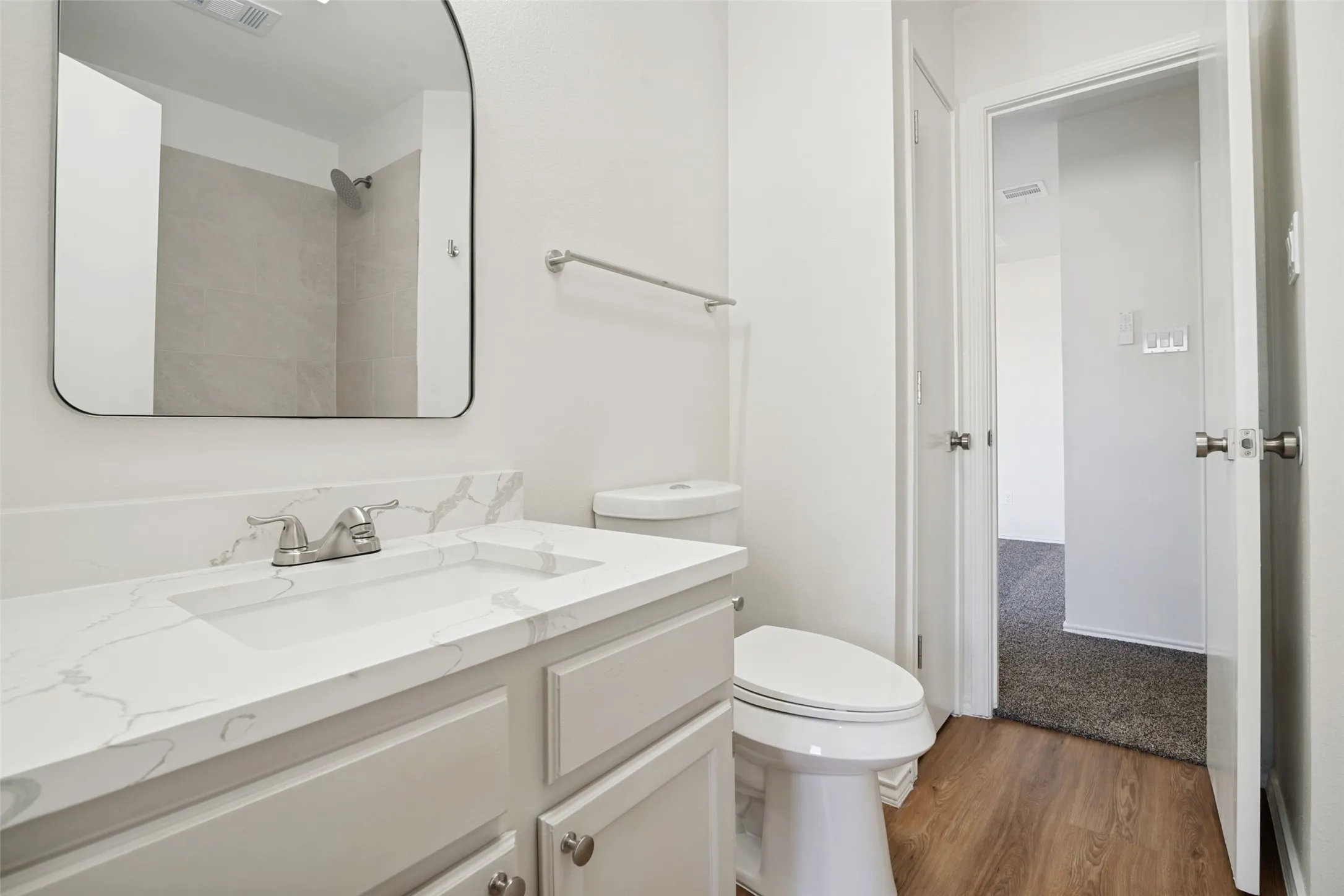 Bathroom featuring a white vanity with an integrated sink, a stone-finish countertop, brushed nickel faucet, and a contemporary frameless mirror