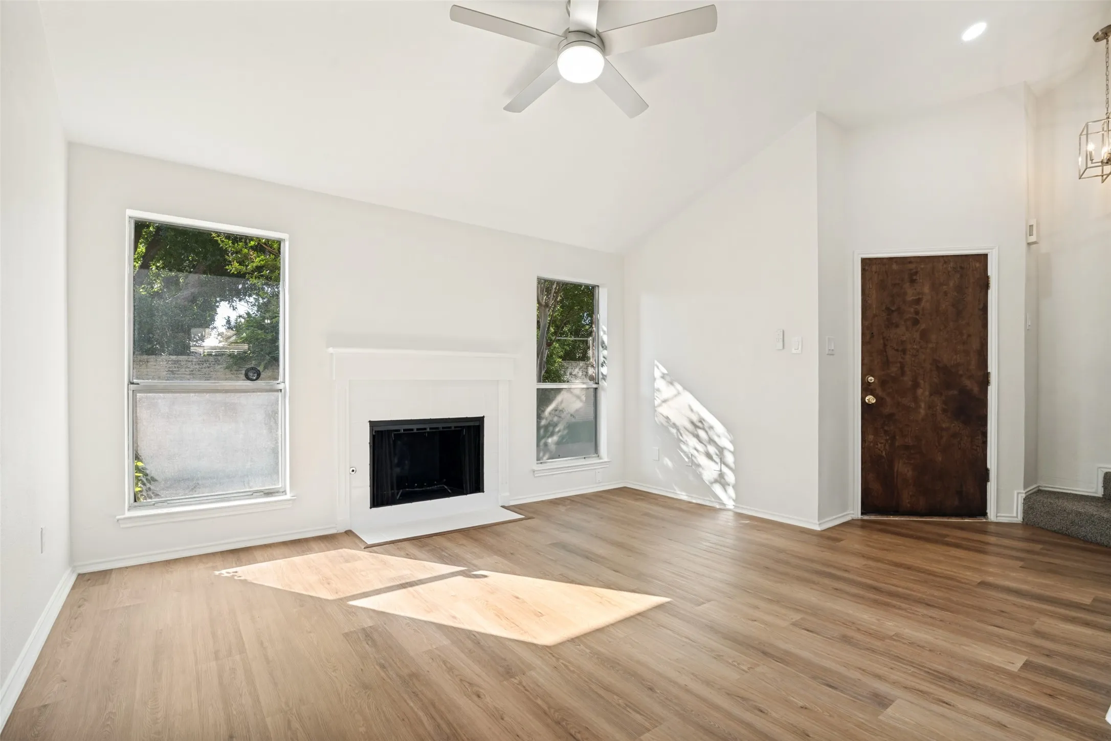 Spacious living area featuring a vaulted ceiling, wood-finish flooring, and a fireplace with a white mantel