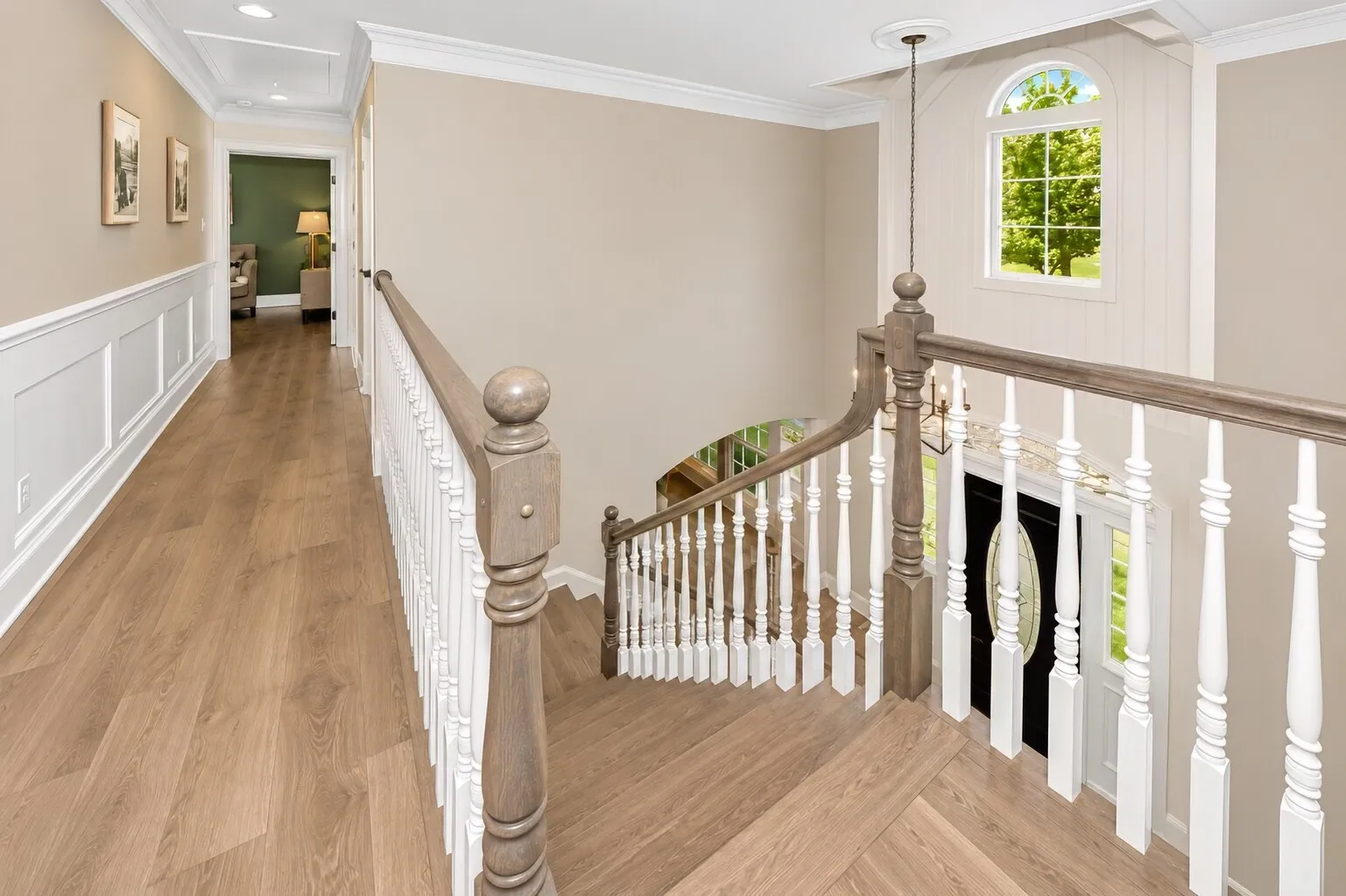 Upstairs opens into a bright, easy-flow landing where natural light pours through the arched window and spills across the wood floors. The open railing keeps the space feeling connected to the foyer below, while the hallway leads quietly into the primary suite and secondary bedrooms. It’s one of those spots in the home that feels calm — a soft pause between spaces — and gives the upstairs a modern farmhouse openness that buyers love.