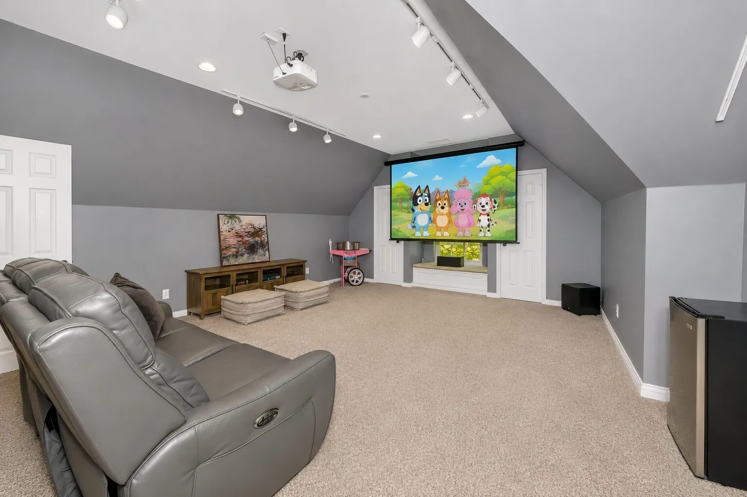 This upstairs media room is set up for easy movie nights and weekend relaxing, complete with three-seat theater recliners, an Epson projector with built-in apps, a remote-controlled screen, and the speakers shown in the photo. Built-in wall speakers make the sound feel immersive, and the receiver is neatly tucked into the left closet for a clean setup. With two closets and its own half bath, the space works beautifully as a dedicated theater, teen hangout, or multipurpose bonus room that stays comfortable and functional.
