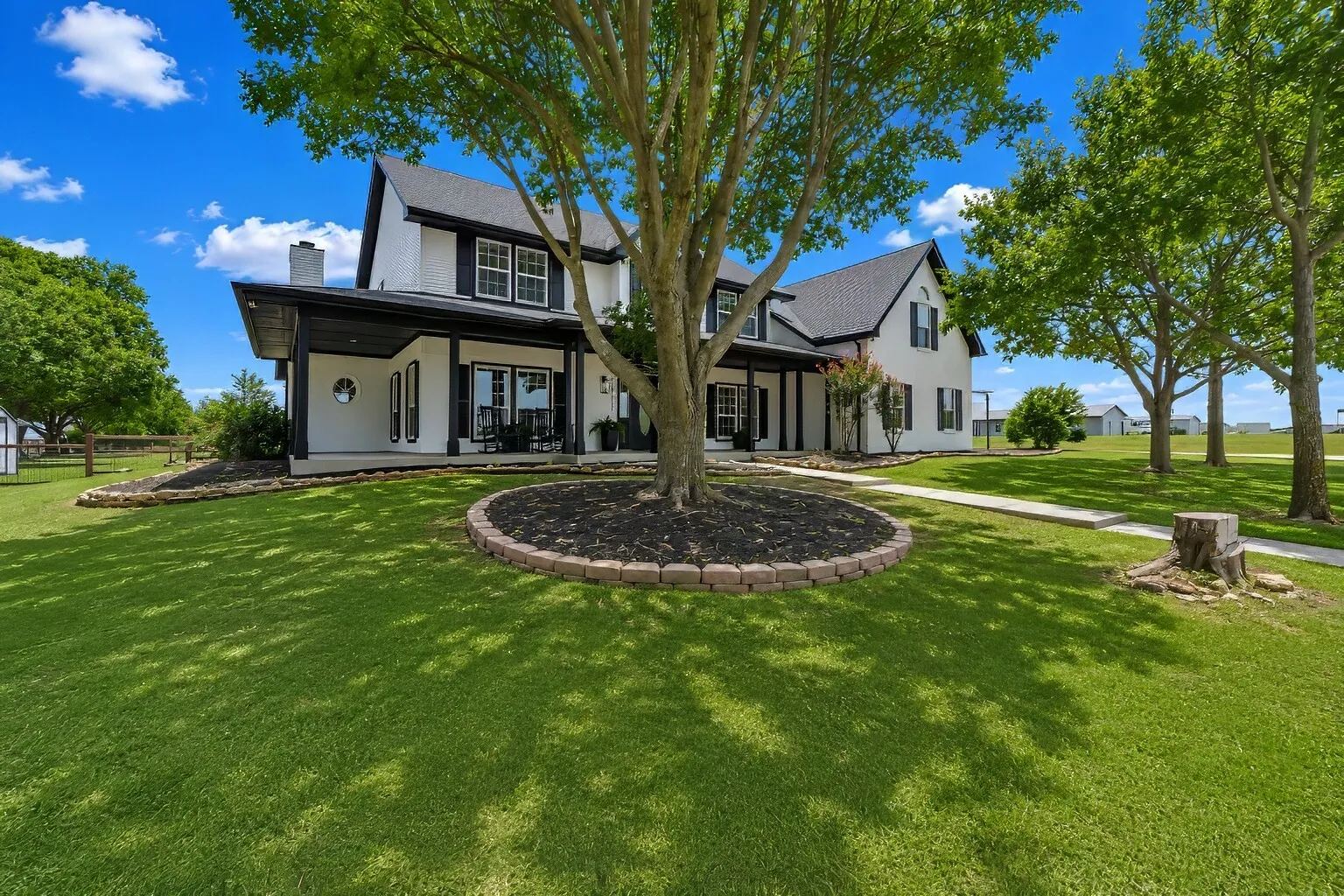 A modern farmhouse framed by wide Texas sky and mature trees, where crisp black-and-white styling meets the easy rhythm of country living. The front porch stretches across the home with simple, welcoming details, offering a quiet place to slow down and enjoy the shade. Clean lines, thoughtful landscaping, and open acreage set the tone for a home that feels both peaceful and beautifully intentional.