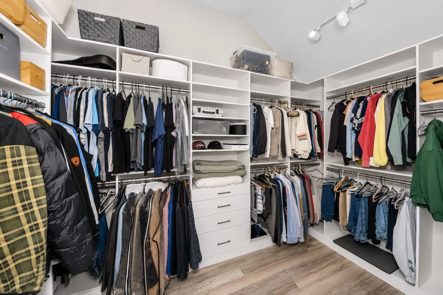 The custom walk-in closet offers generous hanging space, built-in shelving, and dedicated winter storage along the upper sections, keeping everything organized and easy to reach. Bright lighting and a thoughtful layout make the space feel open and functional, with room for clothing, linens, and seasonal items. It’s a well-designed storage area that adds everyday convenience to the primary suite.