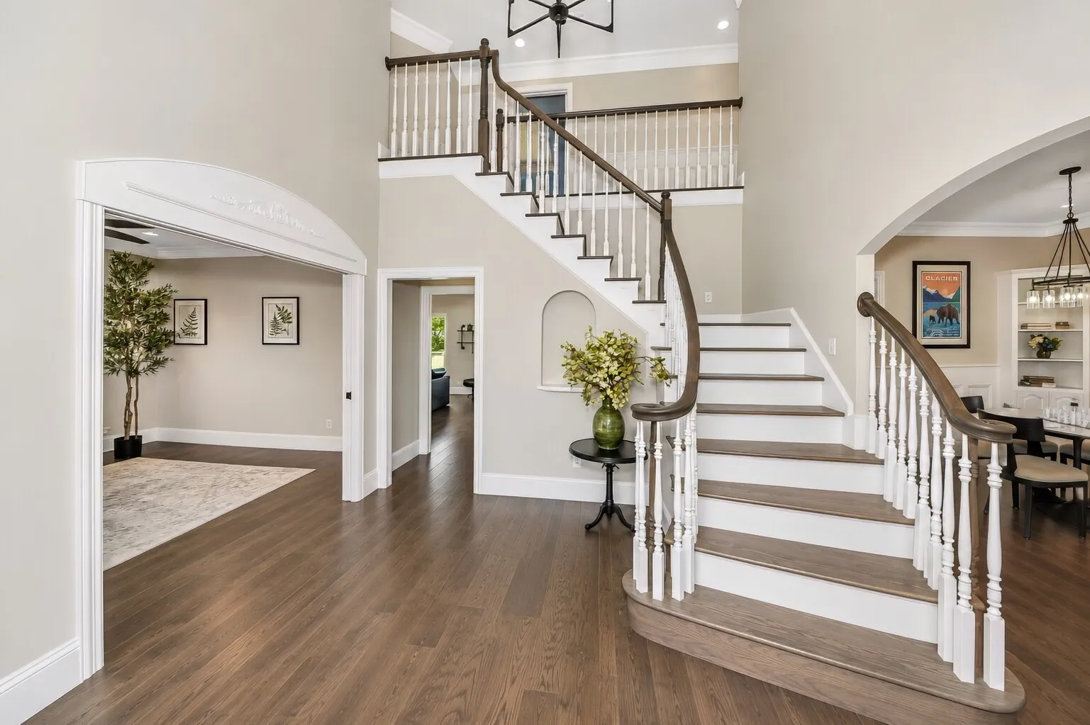 The foyer opens with a bright, easy flow, centered around the curved staircase and clean wood floors. Light moves through the space from every direction, giving the entry a calm, organized feel. The alcove under the stairs adds a simple touch of character, and each doorway leads into rooms that stay open and connected — a welcoming first impression that feels both modern and comfortable.