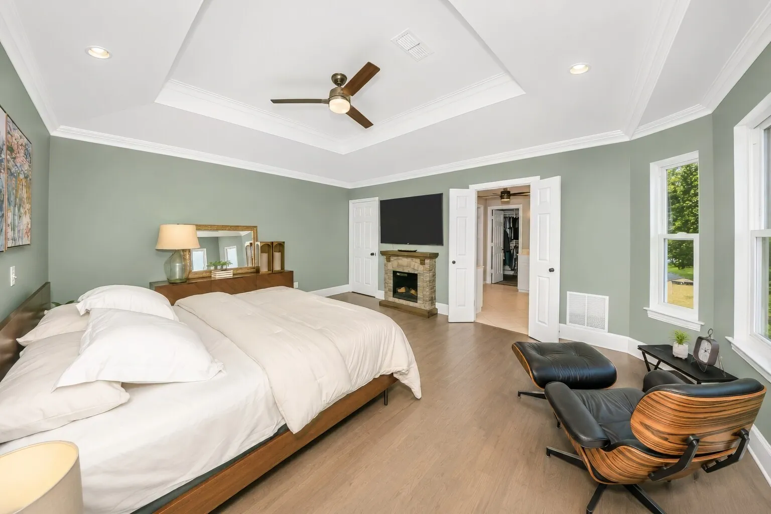 Double doors in the foreground lead into the primary bathroom and the custom walk-in closet, giving the suite a smooth, private flow that feels both spacious and intentional. The bedroom itself is anchored by a king-size layout with a sitting area, soft natural light, and modern farmhouse details that make the space feel calm and retreat-like. Everything you need — from the spa-style bath to the oversized closet — is tucked just steps away, creating a suite that’s easy to live in and easy to love.