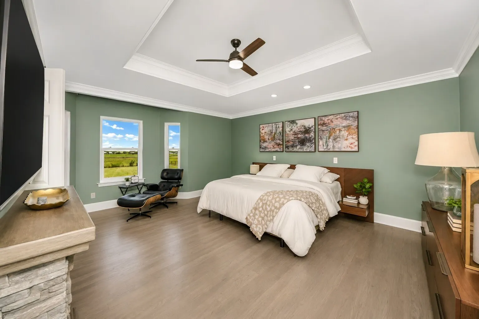 Tucked at the back of the home, the primary bedroom feels calm and spacious, centered around a king-size layout that still leaves plenty of room for a true sitting area. Large windows pull in soft natural light and open to peaceful views, while the tray ceiling adds a touch of modern farmhouse character. It’s the kind of retreat that gives you space to unwind — read, relax, or start the morning slowly — all set apart from the busier areas of the home.