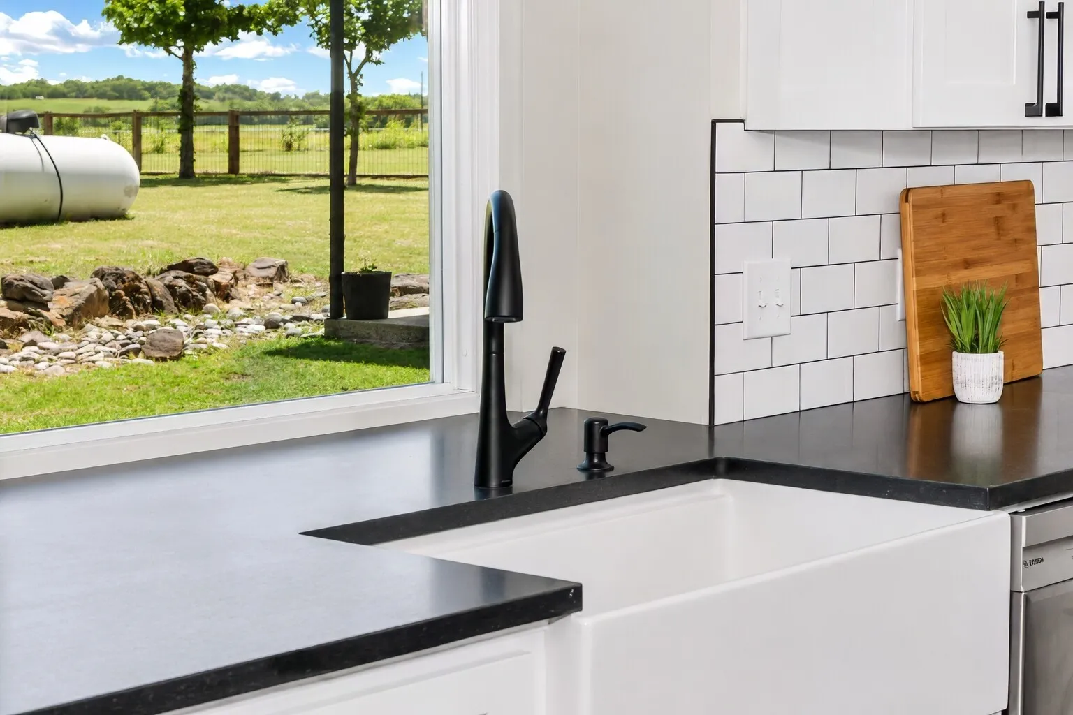 The kitchen’s farmhouse sink sits right under a wide picture window, giving you a clean, modern workspace with a full view of the backyard. Quartz counters, black fixtures, and classic subway tile keep the look fresh and timeless, while the natural light pouring in makes everyday tasks feel a little easier. It’s one of those simple, grounding moments in the home — wash, prep, or pour a cup of coffee while looking out over the open green space.