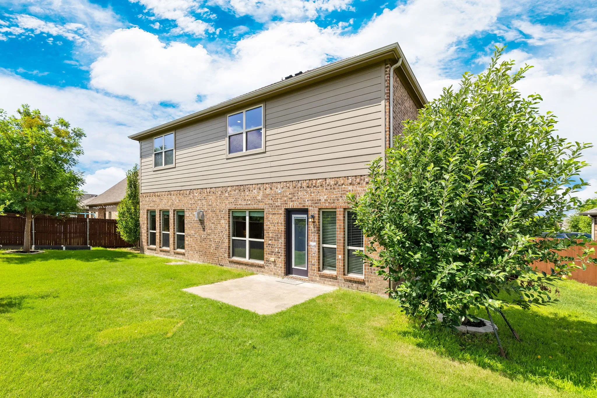 Spacious backyard featuring a concrete patio, verdant lawn, and mature trees