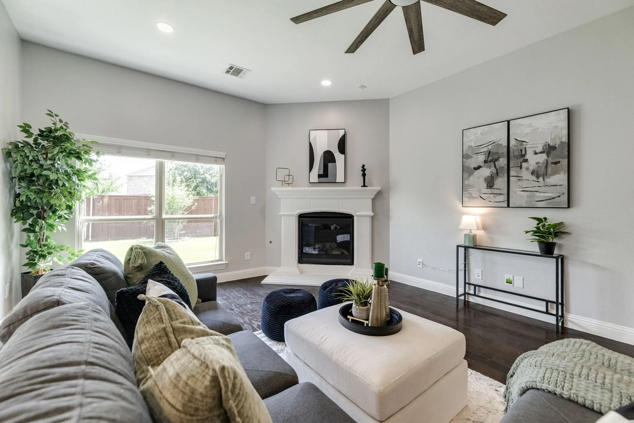 Living area featuring a fireplace with a white mantel, dark wood-finish flooring, recessed lighting, ceiling fan, and a large window overlooking the backyard