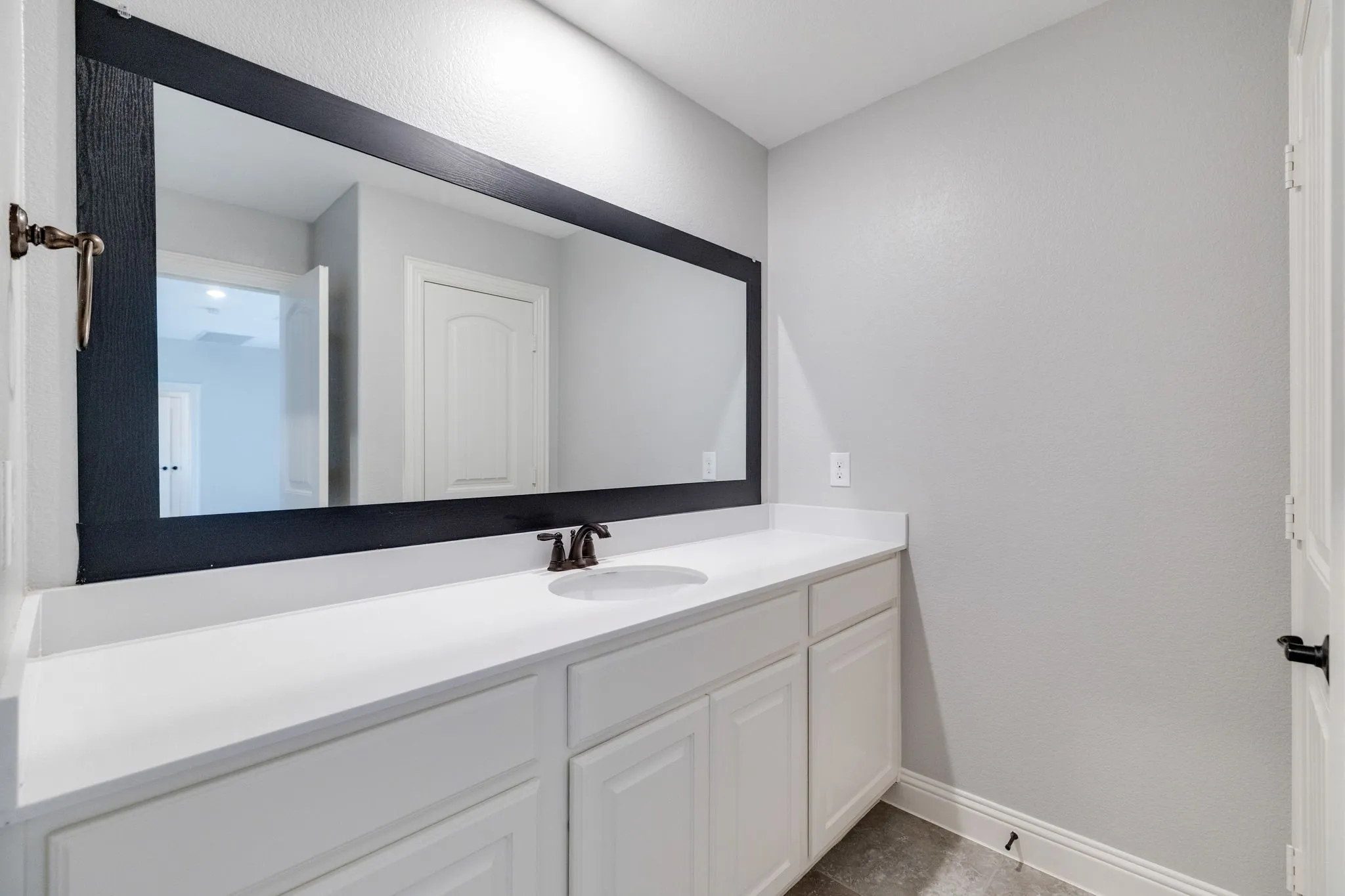 Bathroom vanity featuring a single integrated sink, white cabinetry, a white countertop, and a large wall-mounted mirror with a dark frame