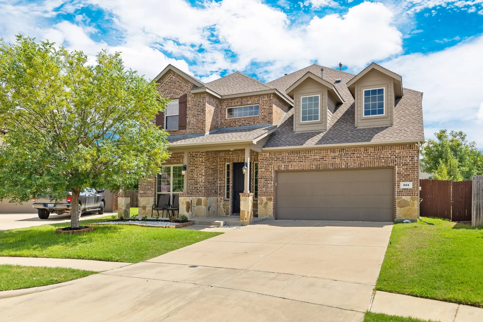 Two-story residence featuring a brick and stone facade, covered porch, attached two-car garage, dormer windows, and a concrete driveway