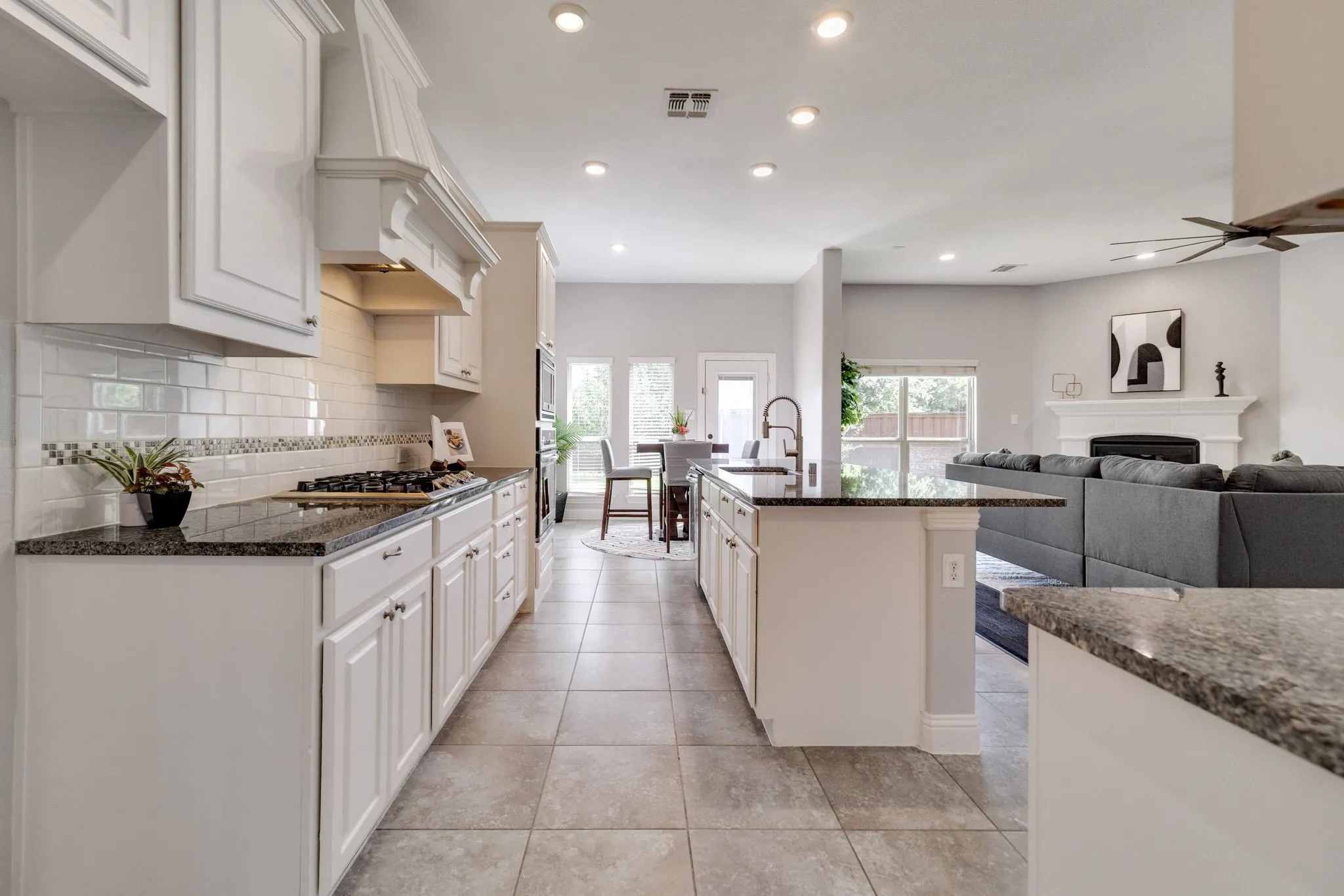 Kitchen featuring white cabinetry, dark granite countertops, subway tile backsplash with decorative accent, a gas cooktop, and a kitchen island with a sink