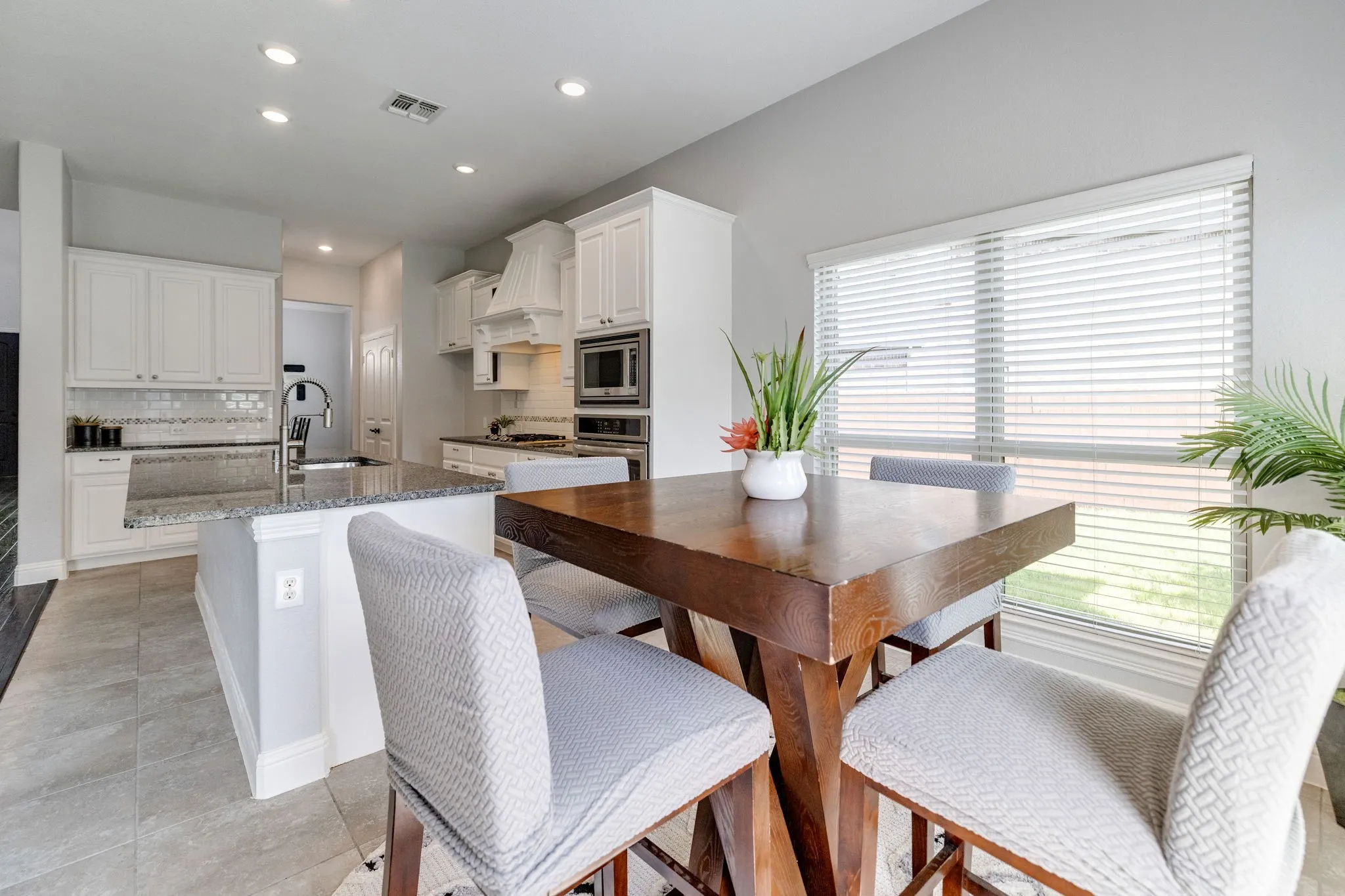 Modern kitchen featuring light cabinetry, tile flooring, recessed lighting, a kitchen island with a double basin sink, and a large window with blinds