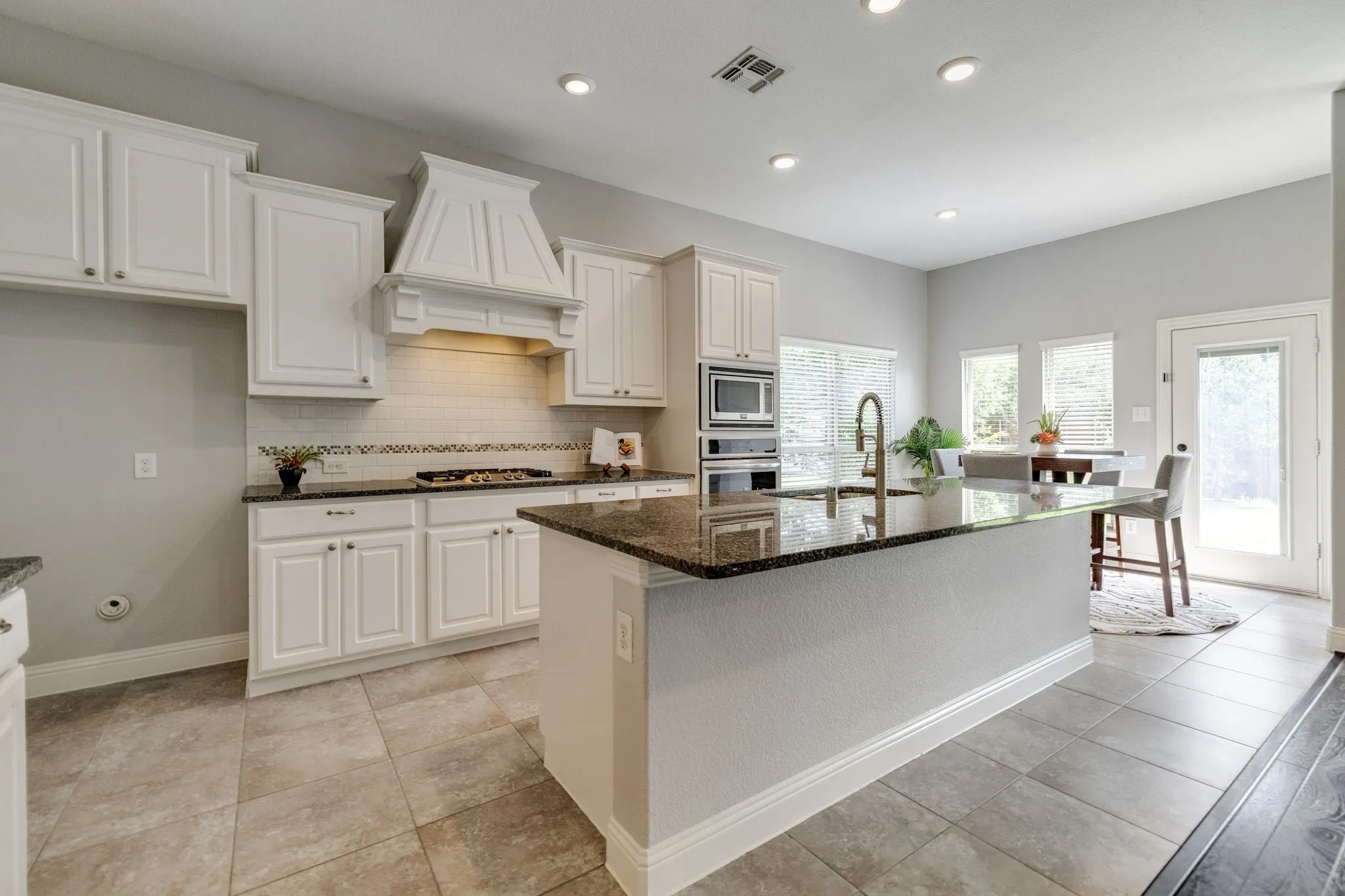 Spacious kitchen featuring an expansive island with a built-in sink, white cabinetry, integrated stainless steel appliances, and tile flooring