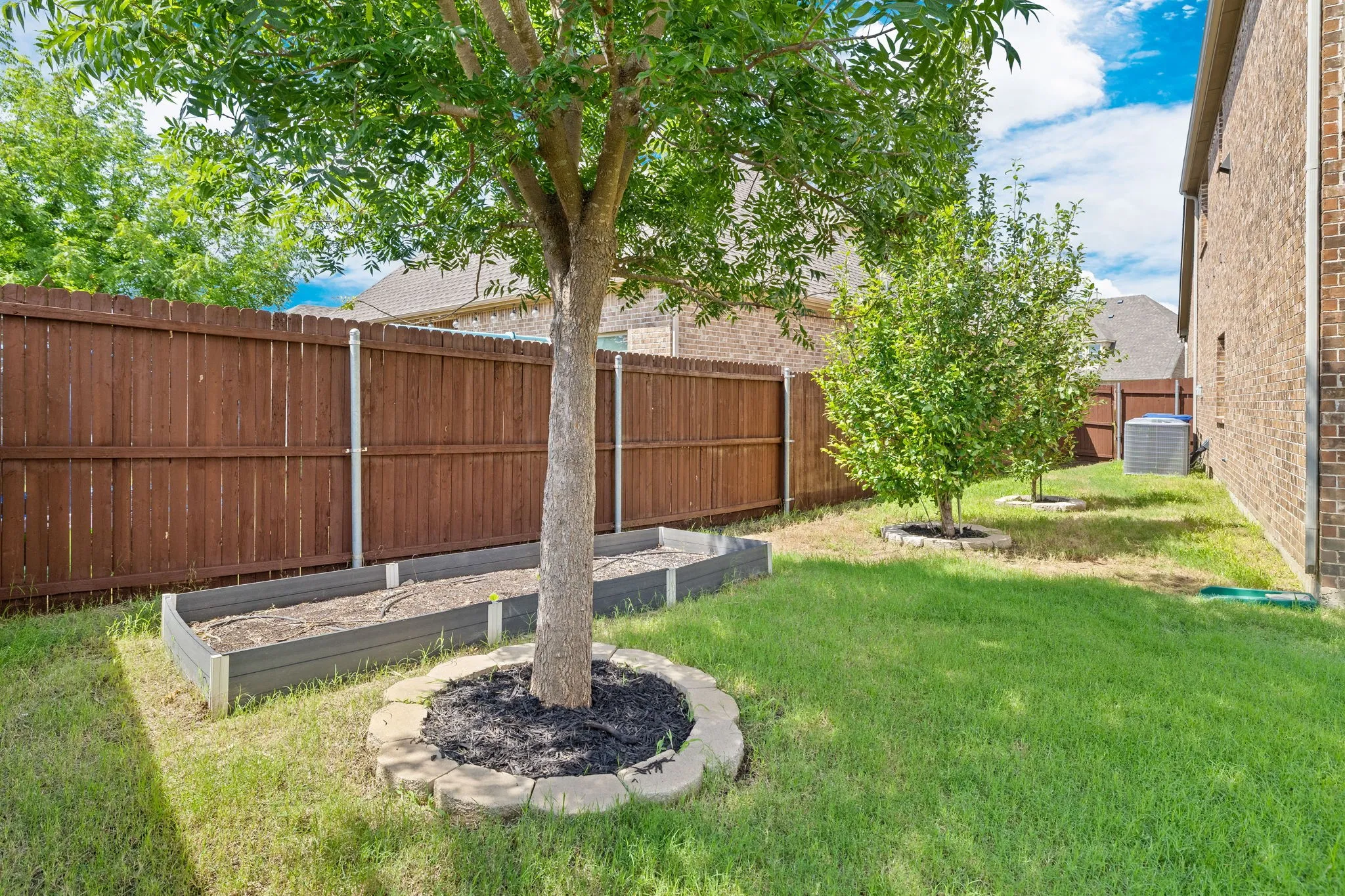 Private backyard with a wood-stained privacy fence, established trees, and raised garden beds