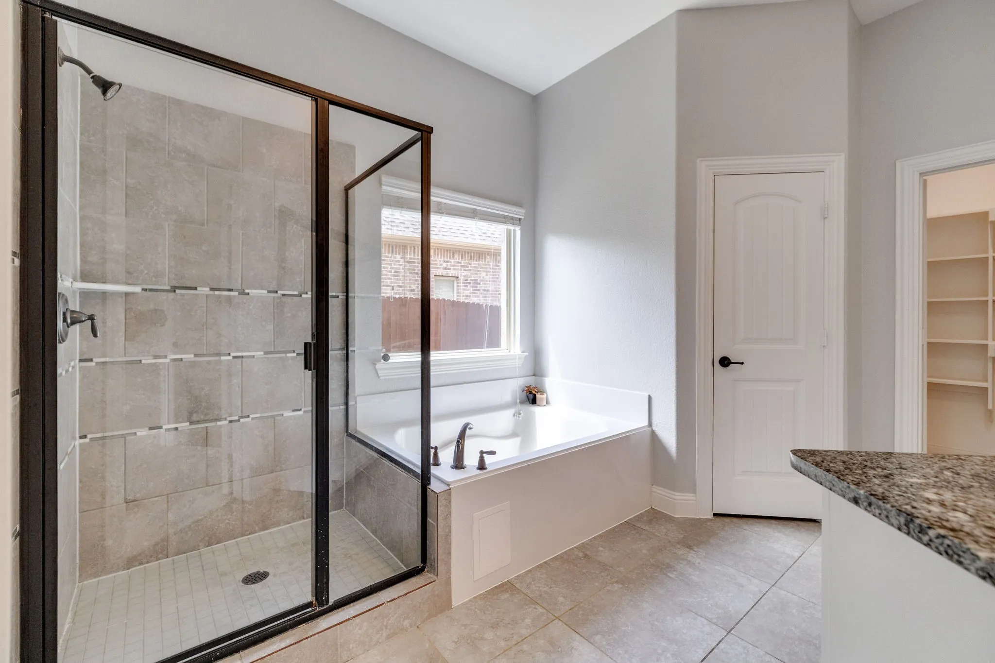 Bathroom featuring a glass-enclosed shower with tile surround, a built-in tub with window, tile flooring, and a countertop with stone finish