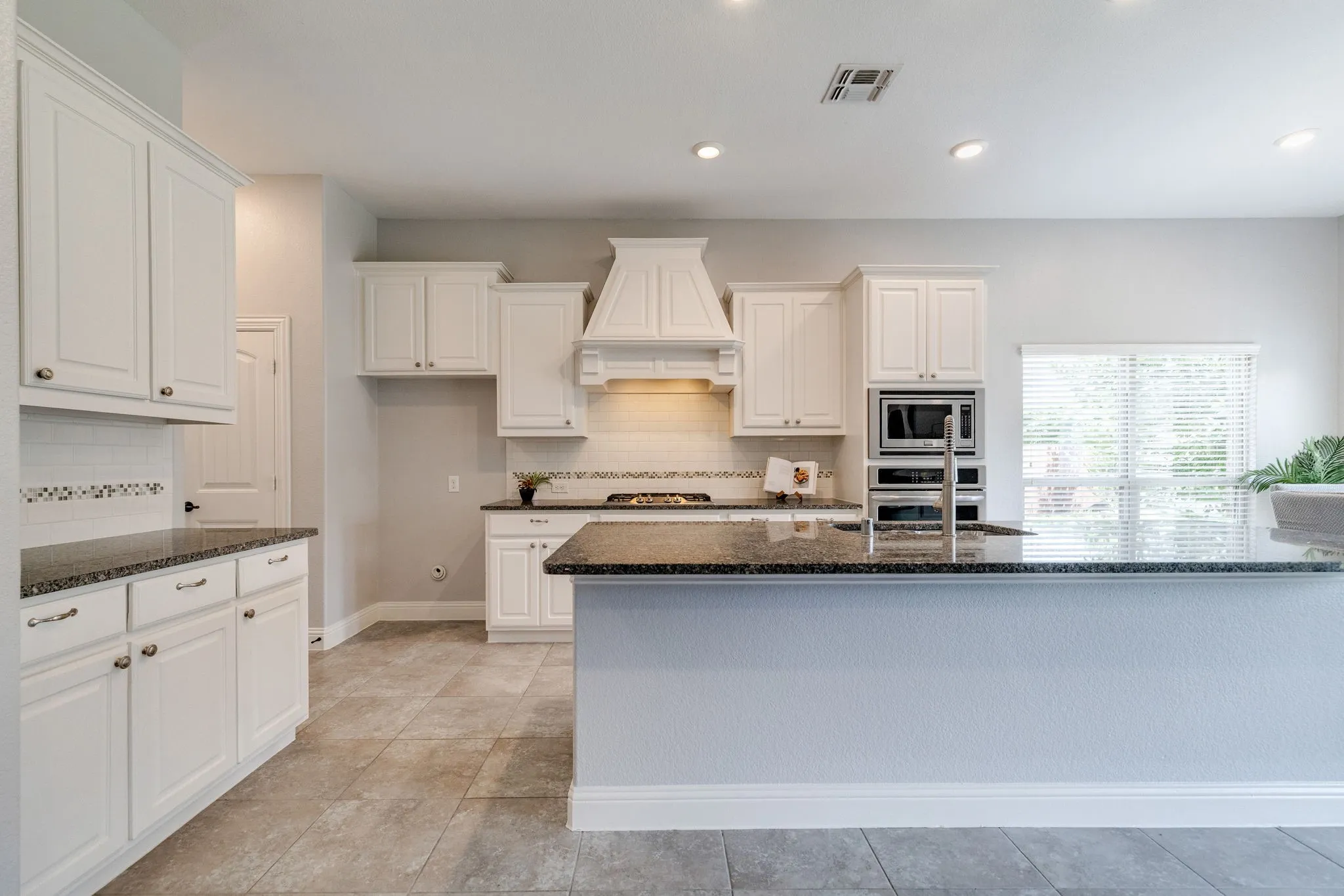 Kitchen featuring white cabinetry with brushed nickel hardware, dark speckled countertops, and a subway tile backsplash with decorative accents