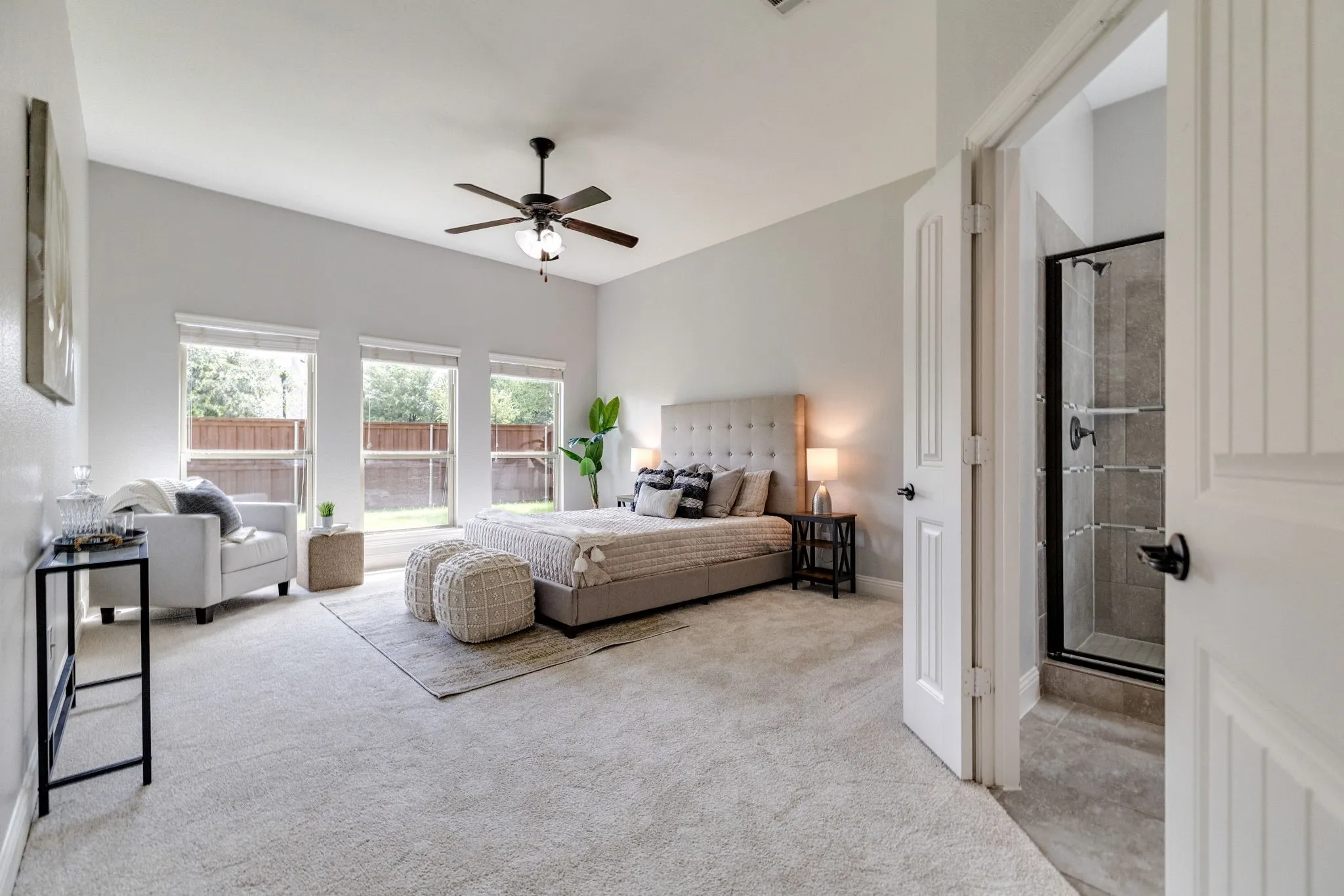 Spacious bedroom featuring light-toned carpeting, three large windows, and a ceiling fan with integrated lighting