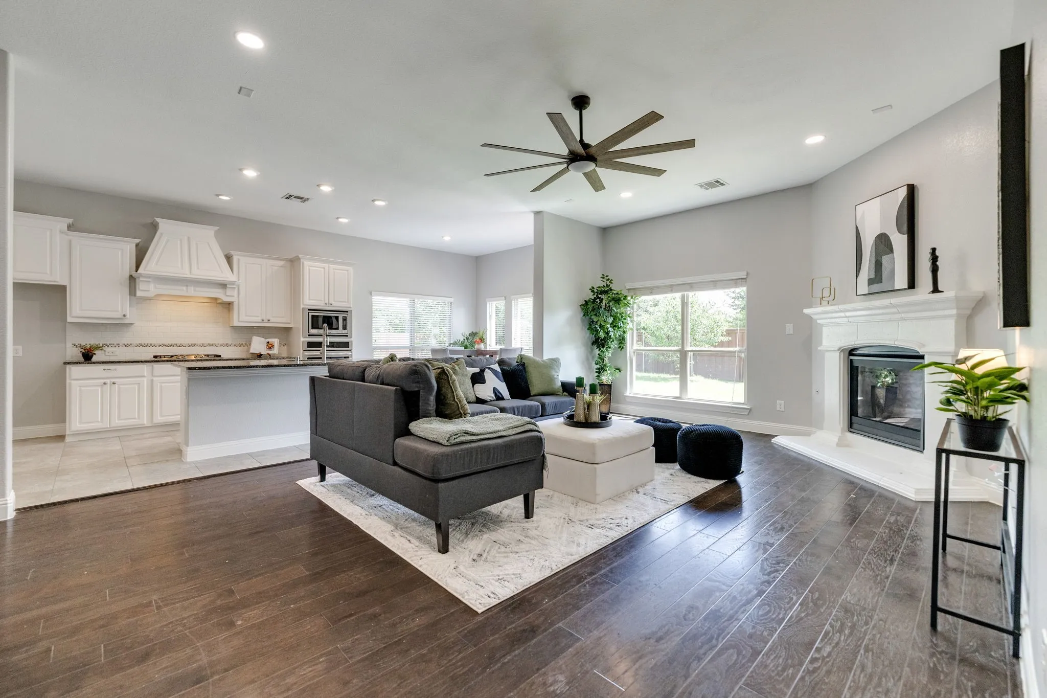 Open-concept living area featuring dark wood-finish flooring, a white mantel fireplace, and a ceiling fan