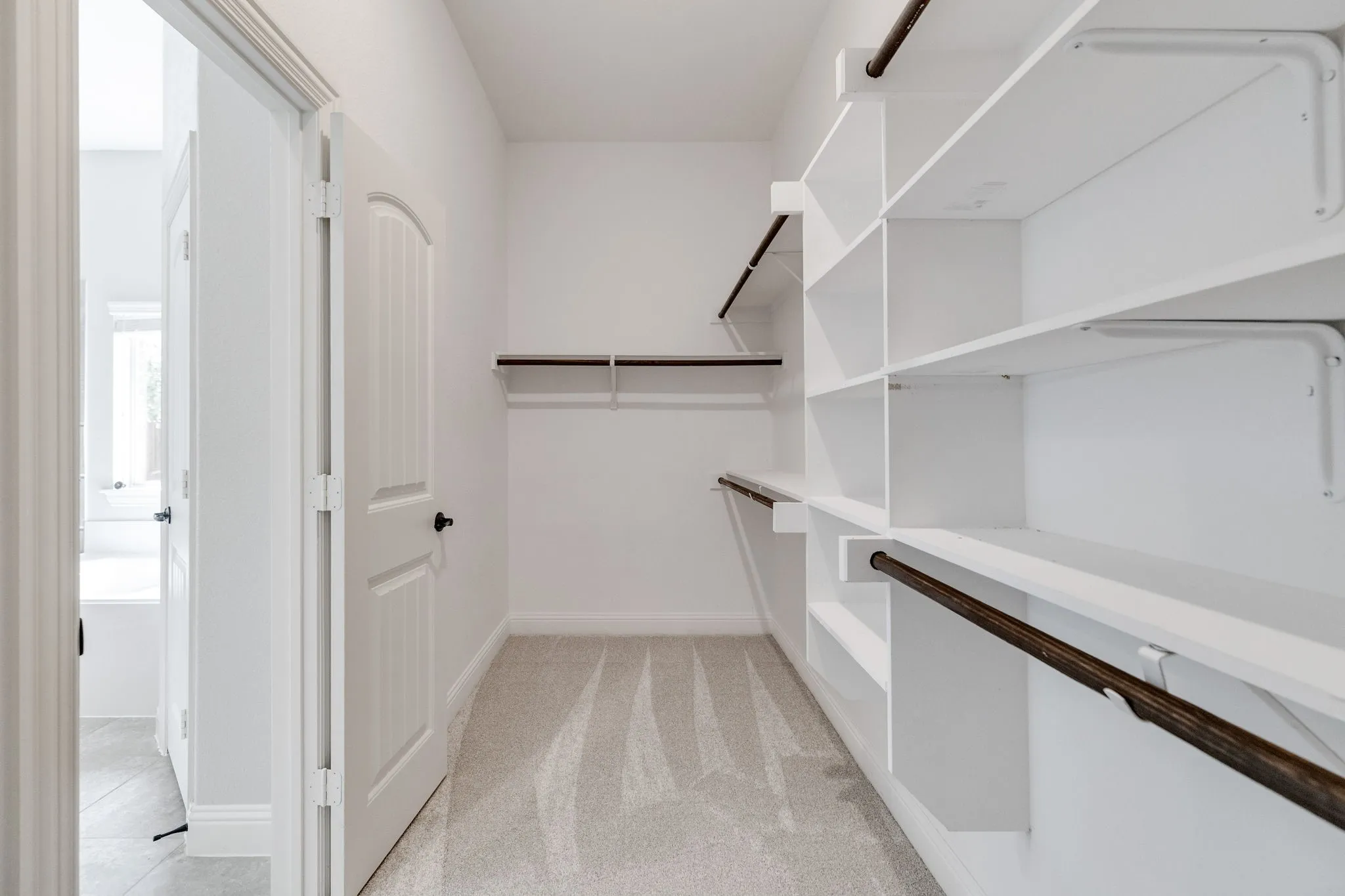 Walk-in closet featuring extensive built-in shelving, multiple hanging rods, light-toned carpeting, and white trim