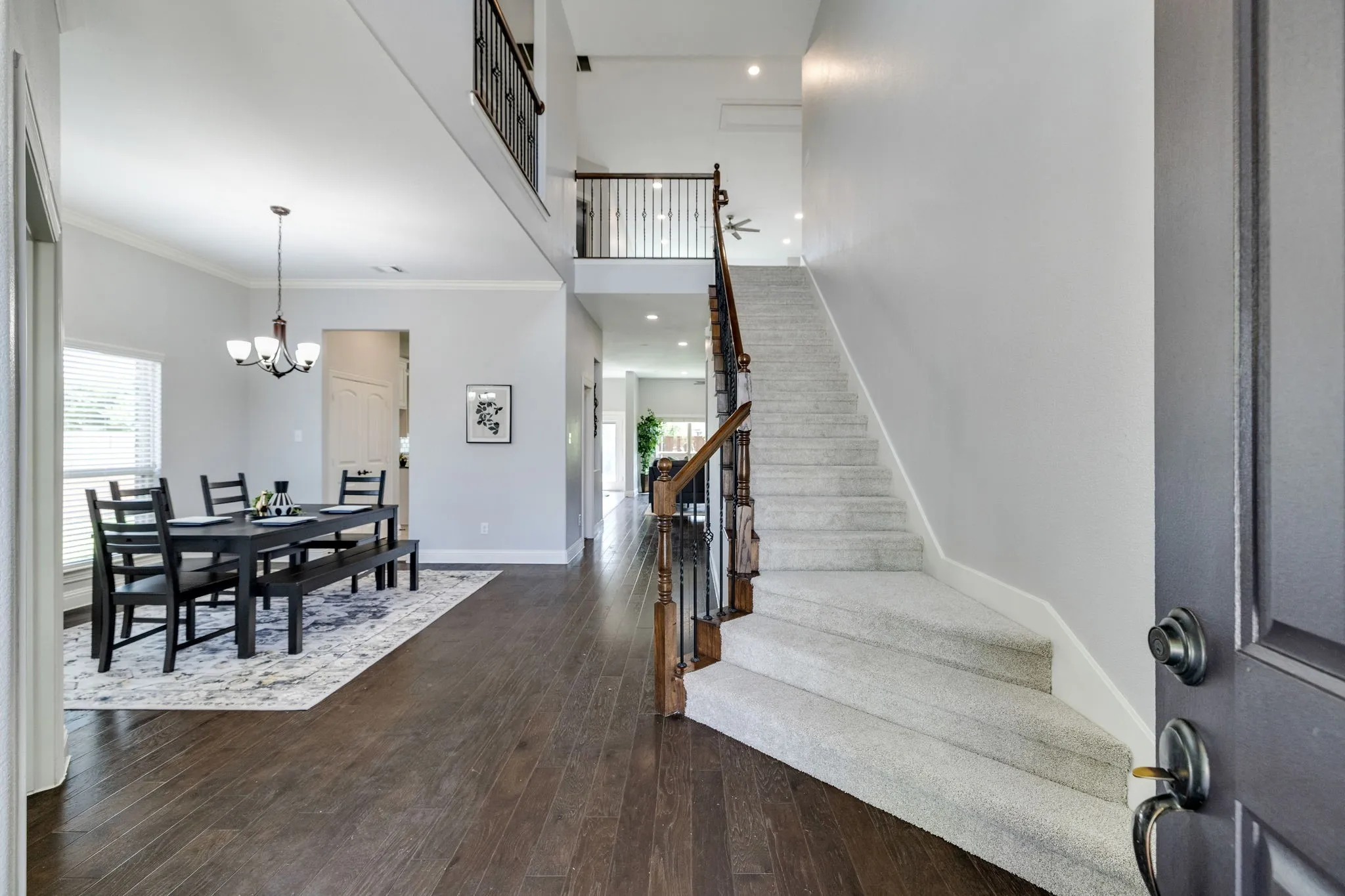 Two-story entry featuring wood-finish flooring, a carpeted staircase with wood and wrought iron banister, and a formal dining area with chandelier