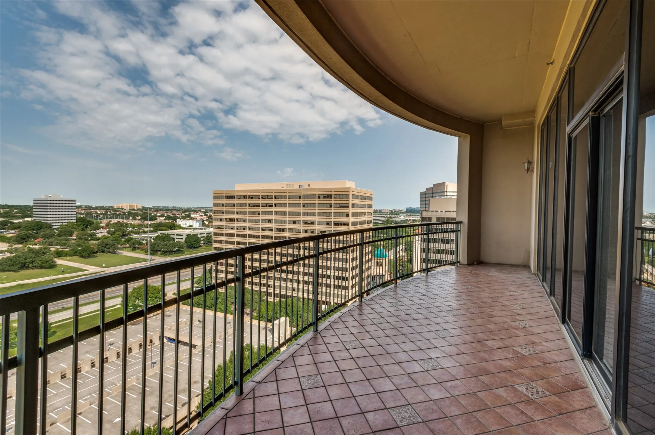 Expansive private curved balcony featuring a black metal railing and terracotta-style tiled flooring with a view of Las Colinas Country Club and the Ritz Carlton.