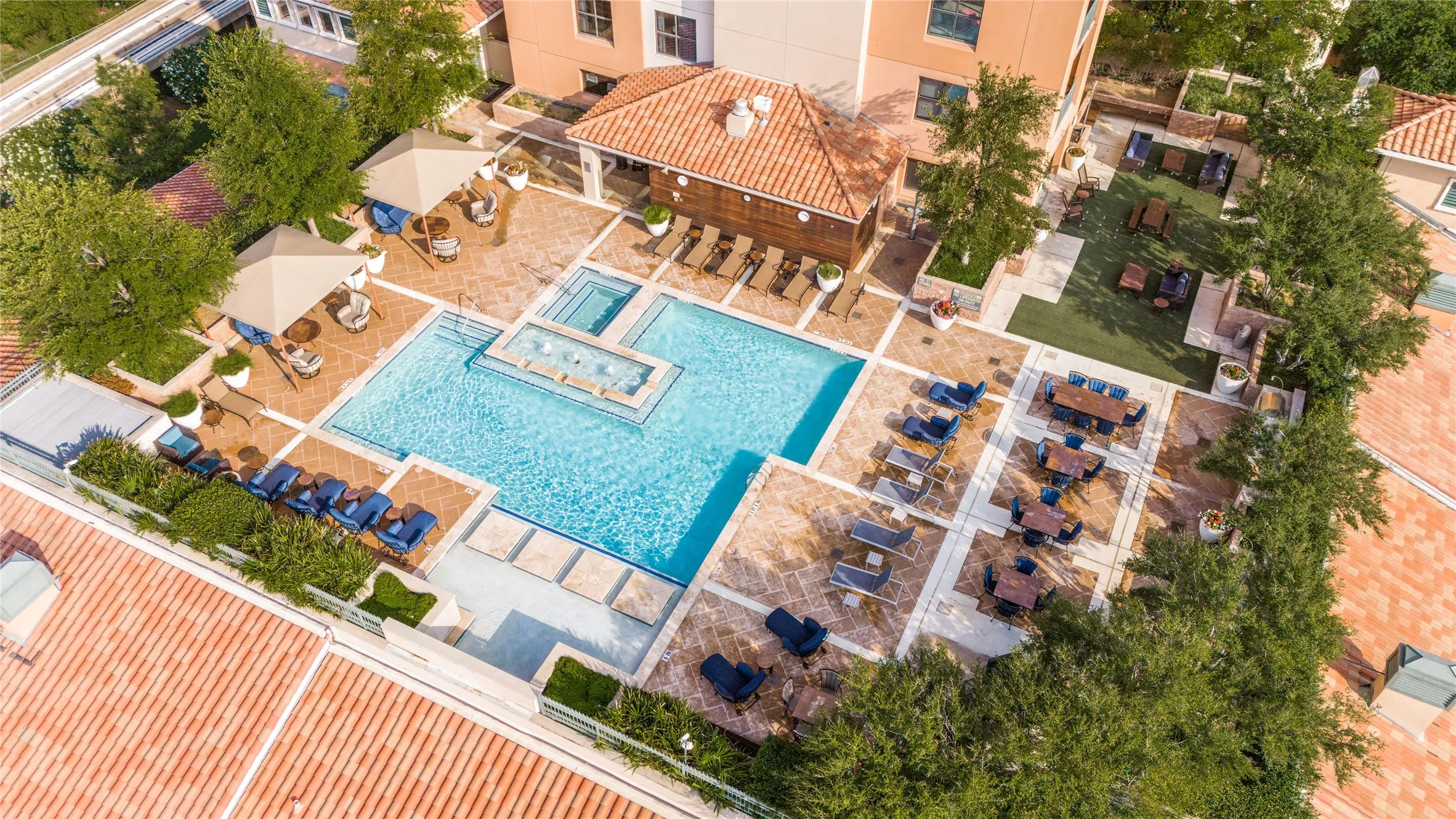 Resort-style outdoor amenity area featuring a rectangular swimming pool with integrated spa and water features, surrounded by a stone paver patio