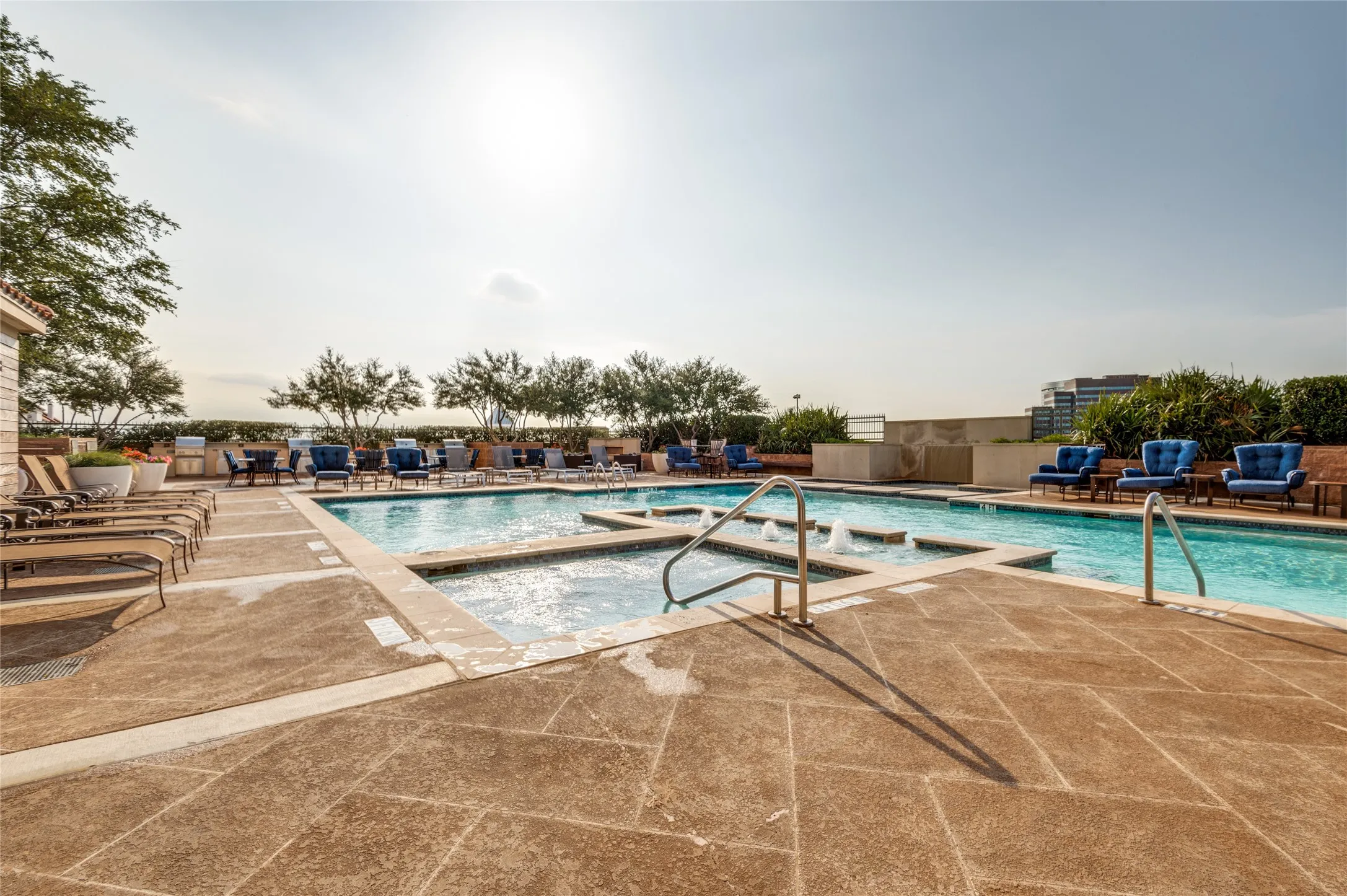 Expansive outdoor pool area featuring a multi-level swimming pool with integrated spa, surrounding stone paver decking, and landscaped perimeter plantings