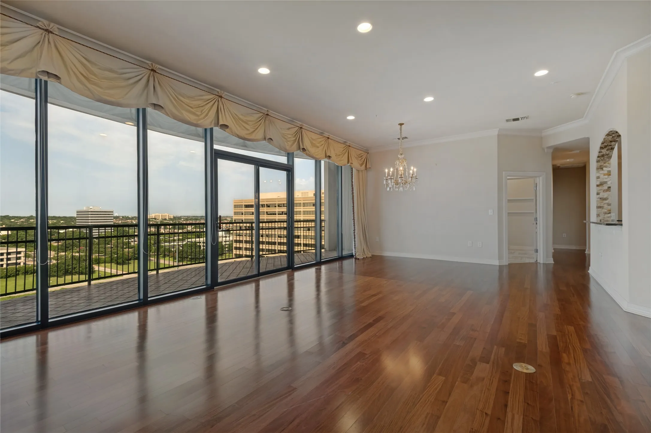 Spacious living area featuring expansive floor-to-ceiling windows, wood-finish flooring, recessed lighting, crown molding, and a chandelier