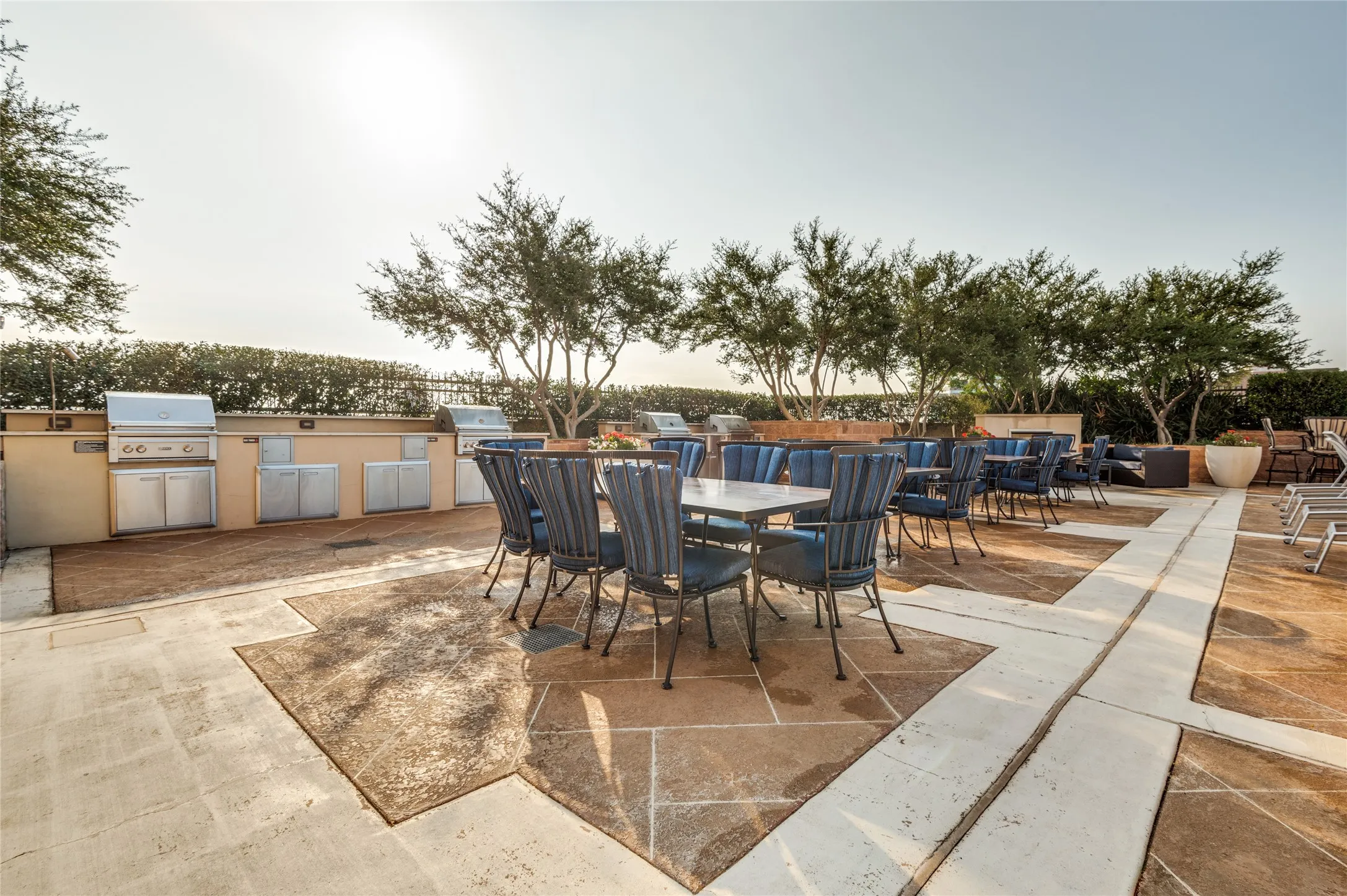Outdoor patio featuring multiple built-in grills, integrated cabinetry, patterned paving, and landscaping