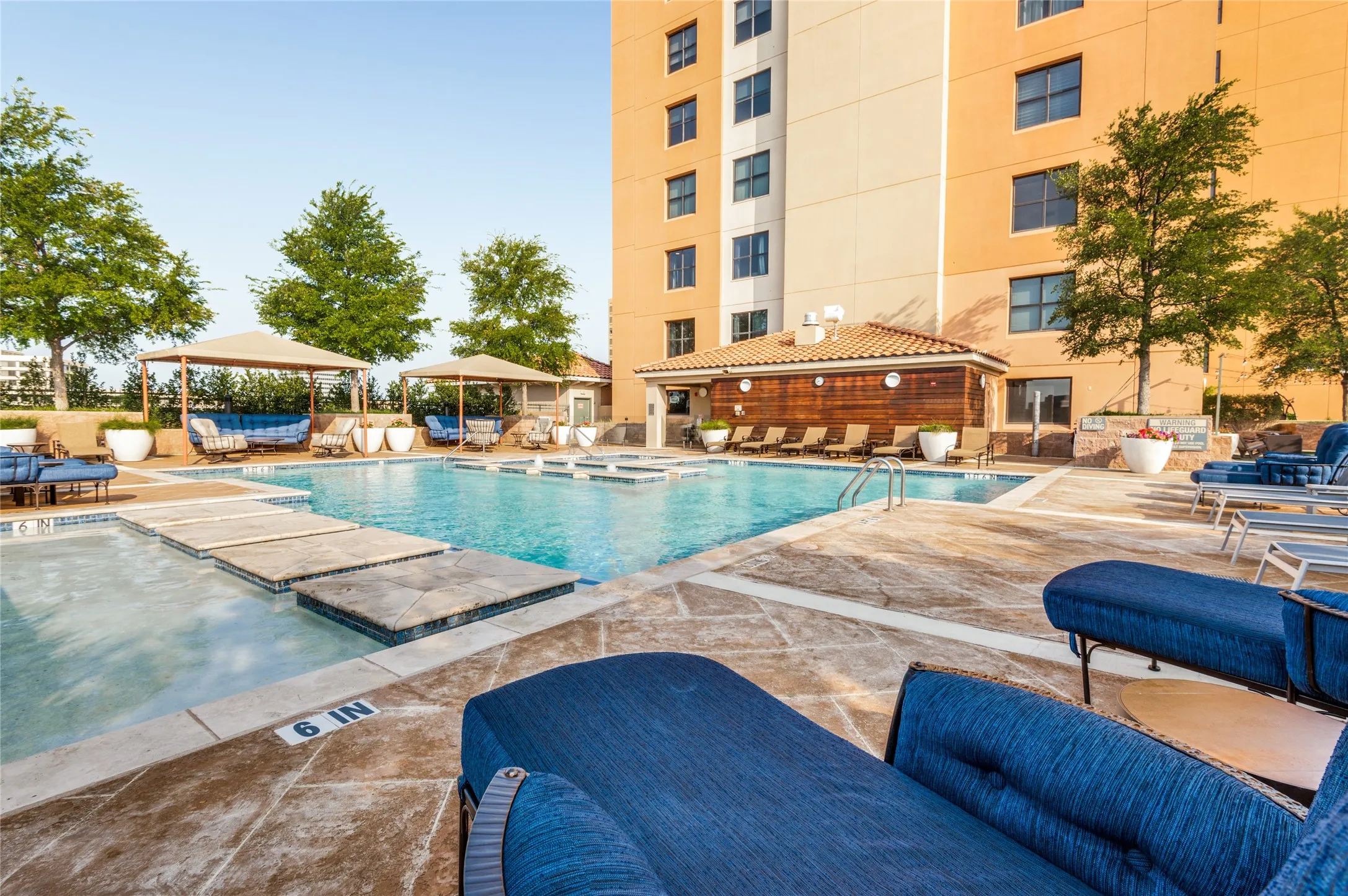 Outdoor pool area featuring a large swimming pool, multiple shaded lounge areas, and a tiled pool house