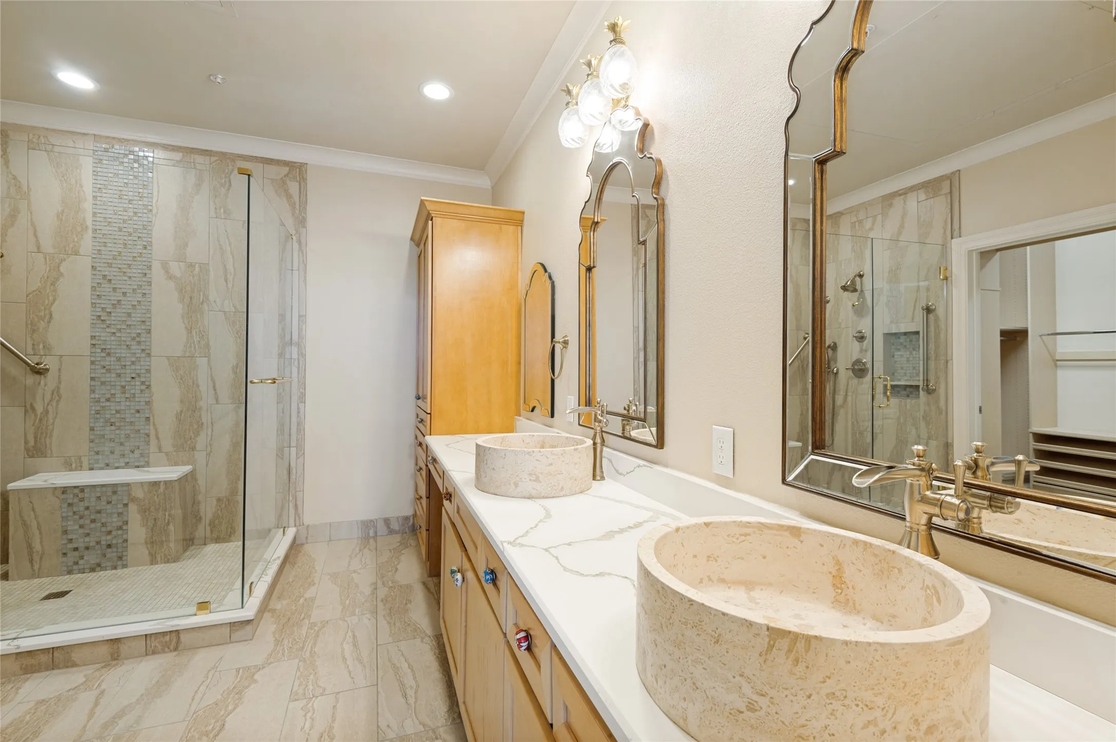Bathroom featuring a dual vanity with stone vessel sinks, light wood-finish cabinetry, and a spacious glass-enclosed shower with a built-in bench