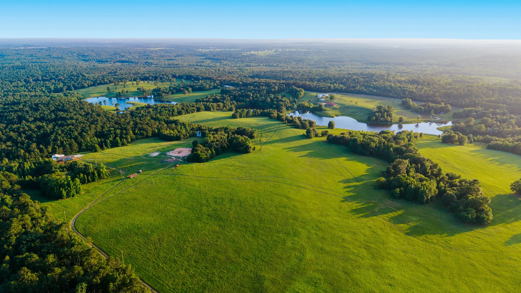 Expansive green pastures and wooded acreage featuring multiple bodies of water