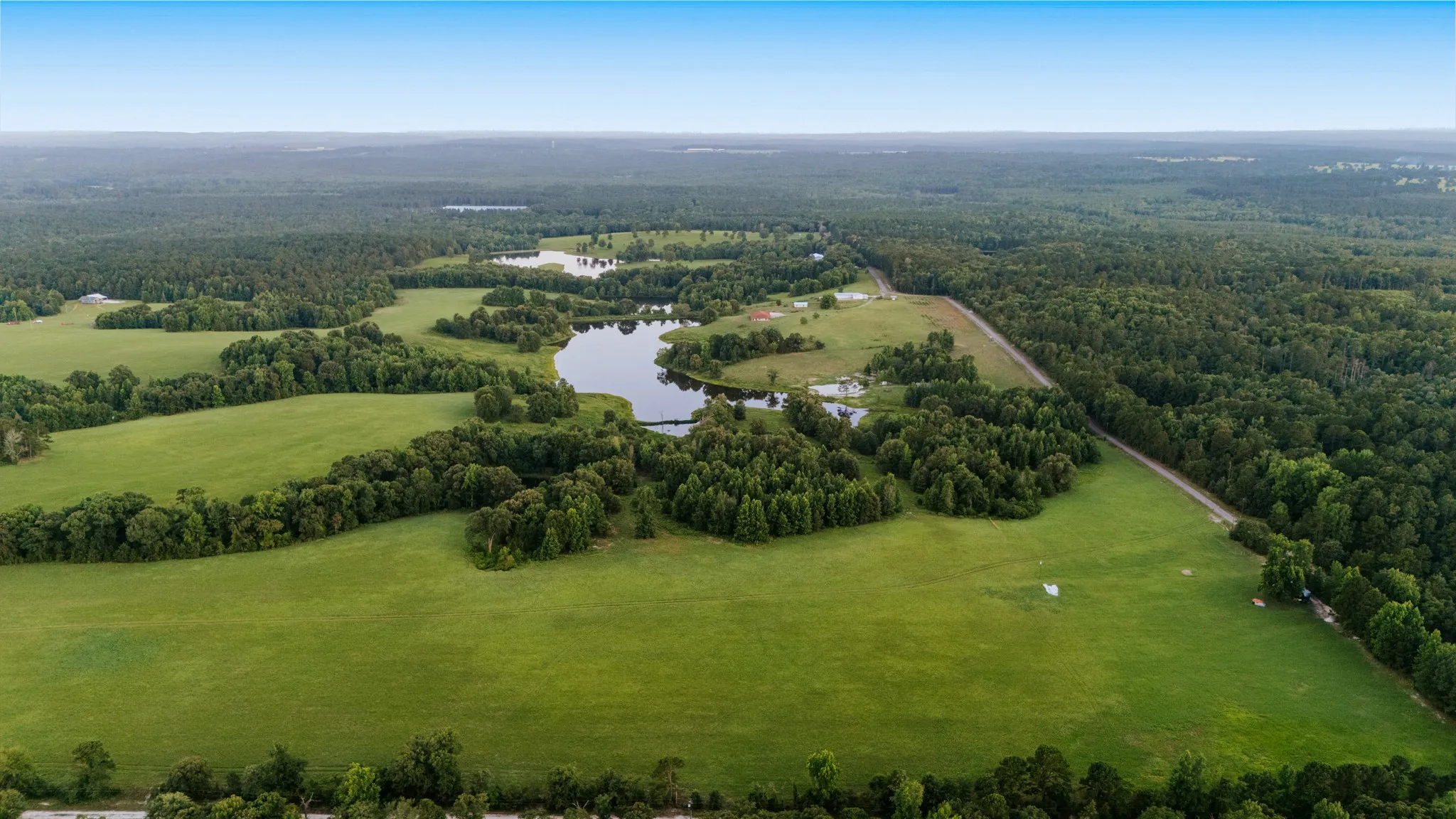 Expansive rural landscape featuring multiple clearings, wooded areas, and natural water features