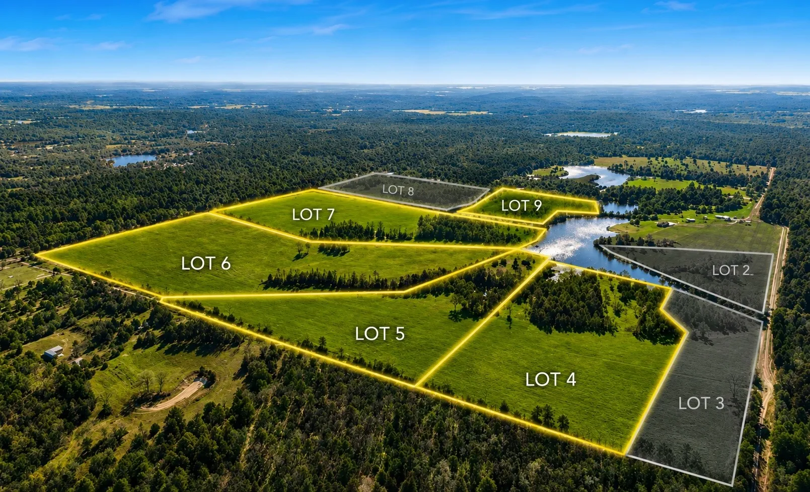 Aerial perspective showcasing multiple land parcels, including verdant fields, a significant body of water, and surrounding wooded areas