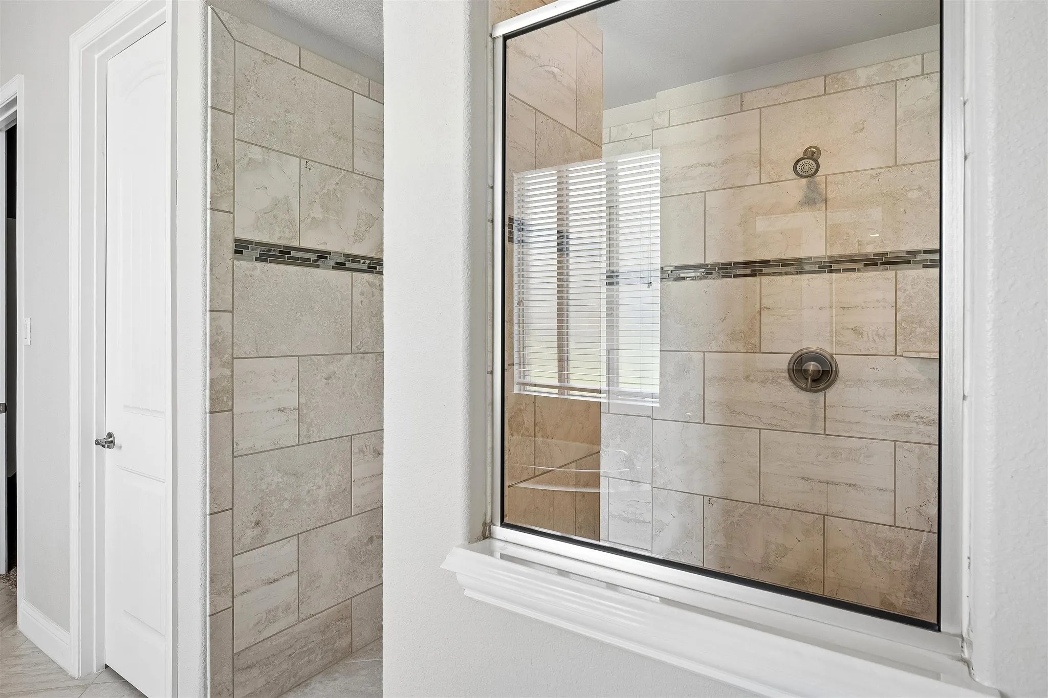 Walk-in shower featuring light-toned large format tile, a decorative mosaic accent band, and a glass enclosure