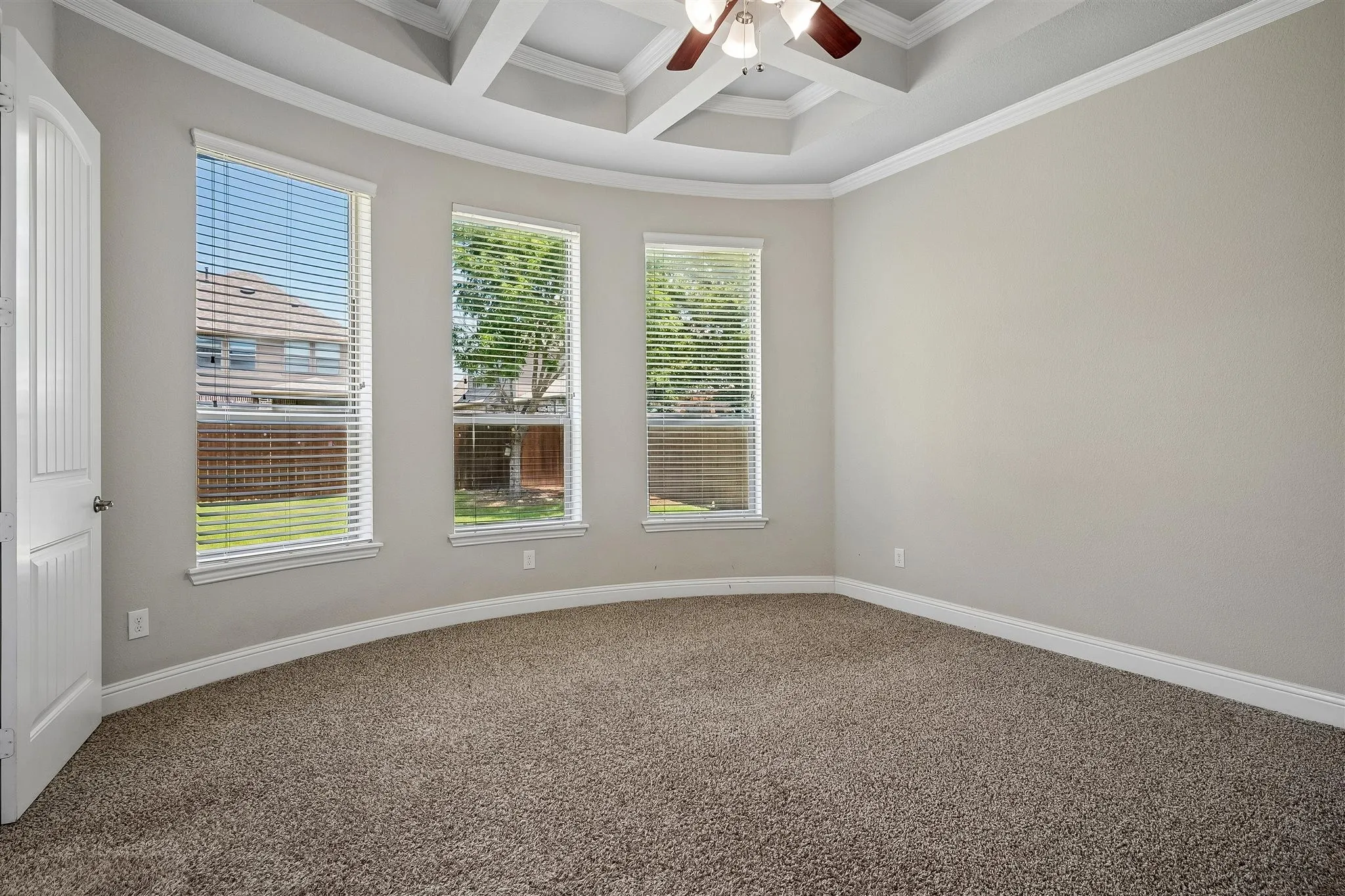 Room featuring curved wall with three windows, tray ceiling, and ceiling fan