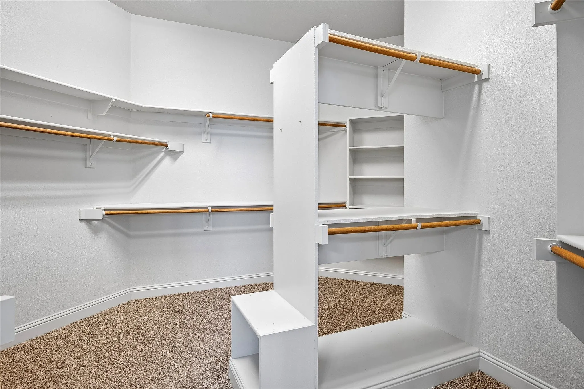 Primary bedroom closet - Spacious walk-in closet featuring built-in white shelving, multiple clothing rods, integrated cubbies, and textured carpet flooring