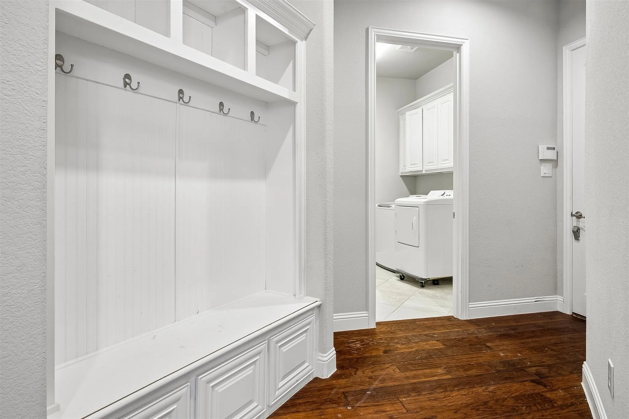 Built-in white storage unit featuring a bench, shelving, and coat hooks