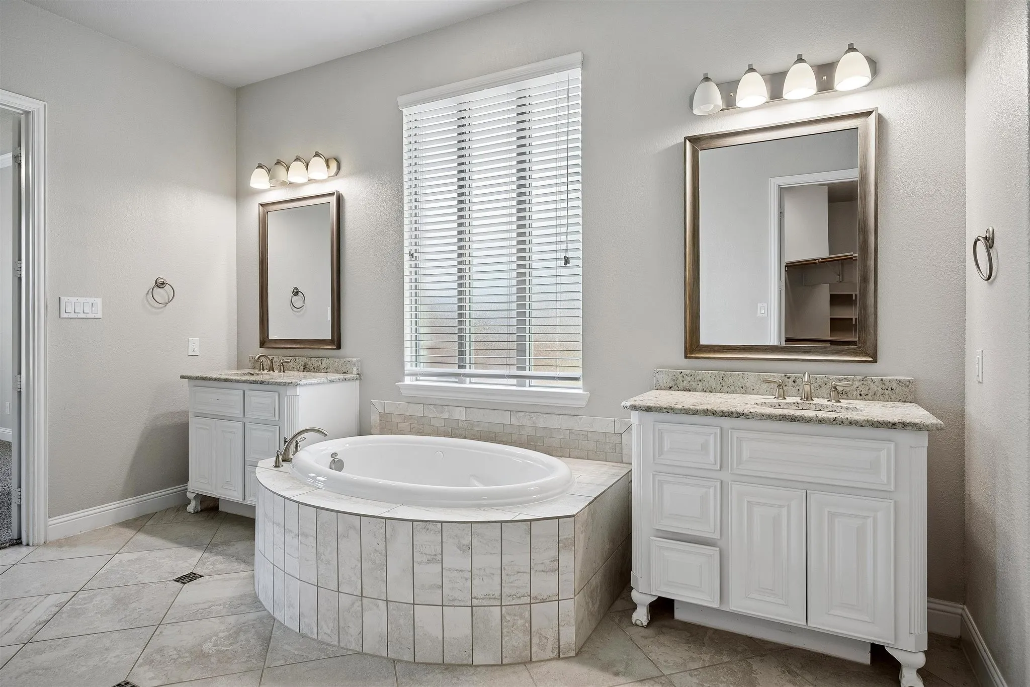 Bathroom featuring a tiled soaking tub and dual white vanities with granite countertops