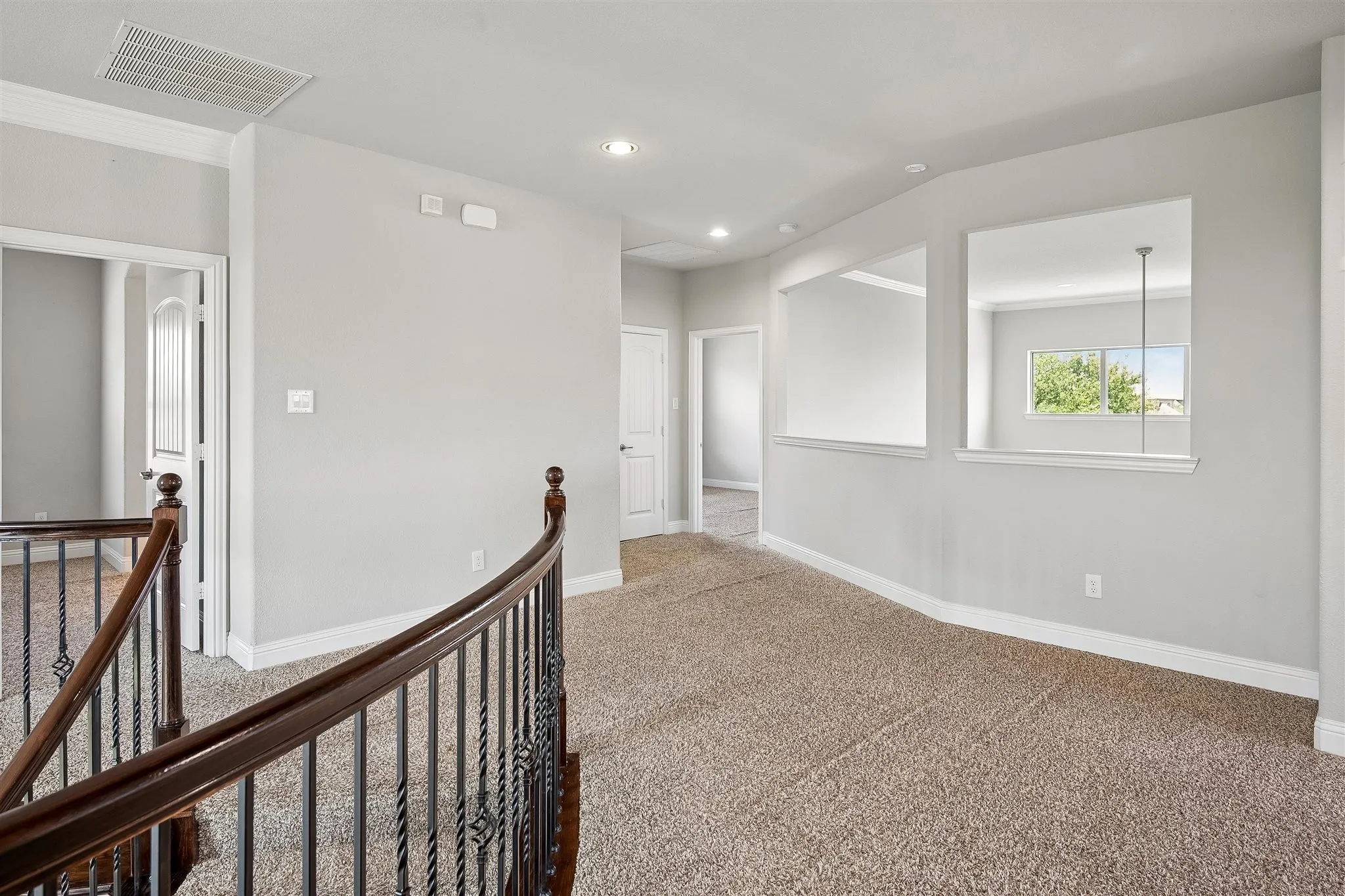 Second-story landing featuring neutral carpeting, light gray walls, white baseboards, recessed lighting, and a dark wood and wrought iron staircase railing