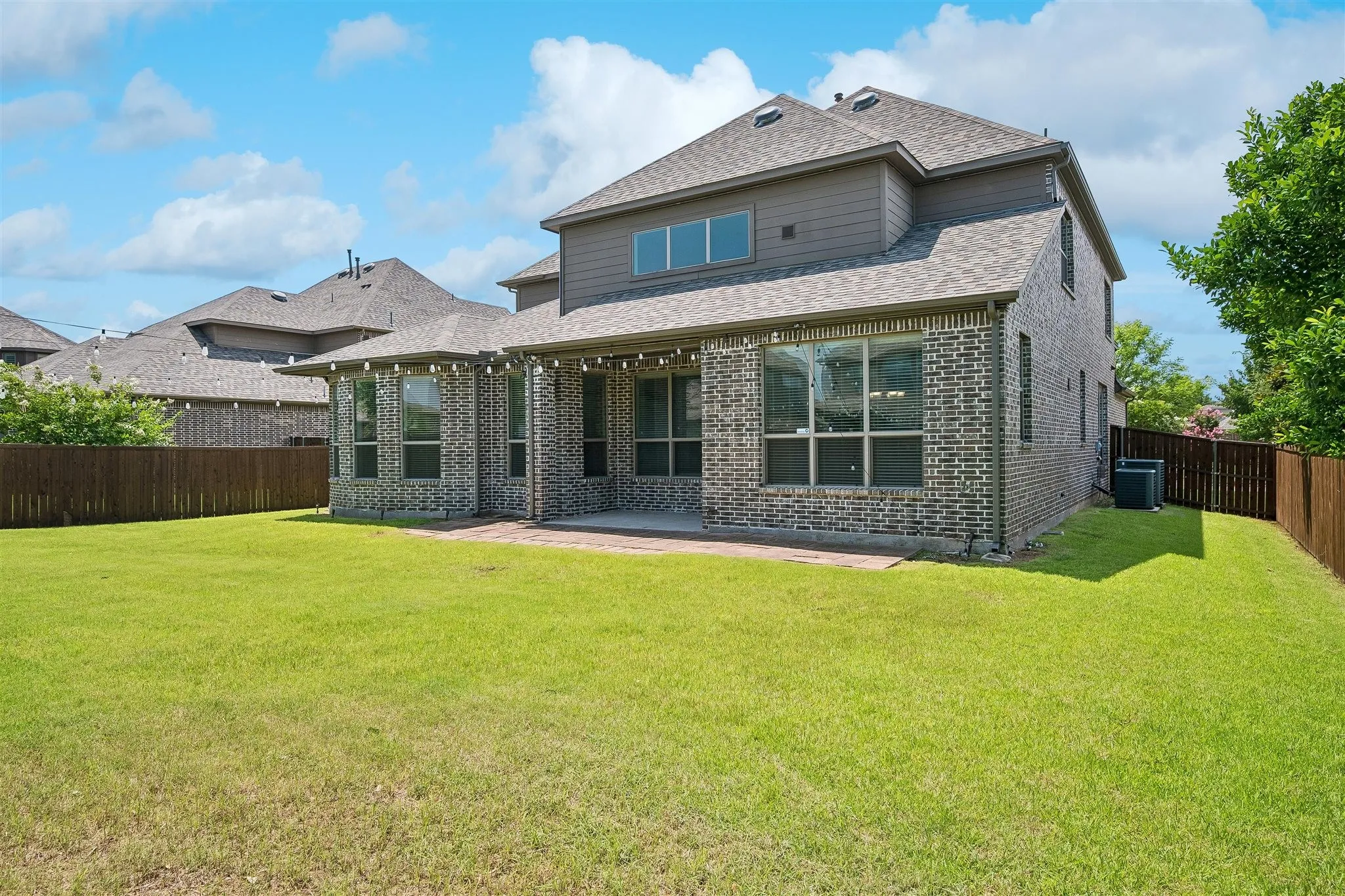 Pool size yard - Expansive green lawn bordering a brick and siding exterior, featuring a covered patio, multiple large windows, and a wood privacy fence
