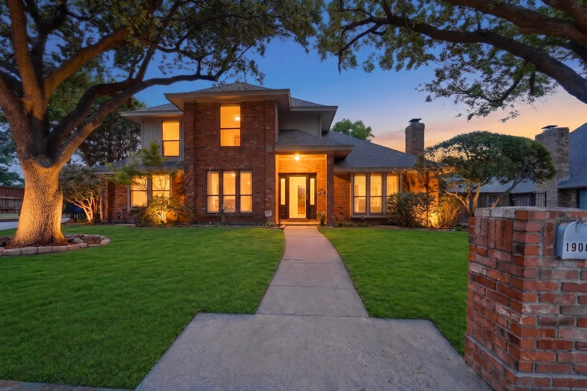 Brick exterior with multiple architectural elements, including a prominent entryway, a large front lawn, mature trees, and a brick mailbox with integrated house numbers