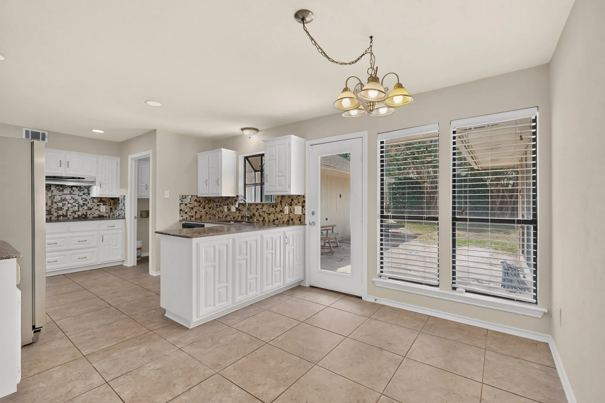 Kitchen and dining area featuring tiled flooring, white cabinetry with decorative paneling, mosaic tile backsplash, and ample natural light from multiple windows