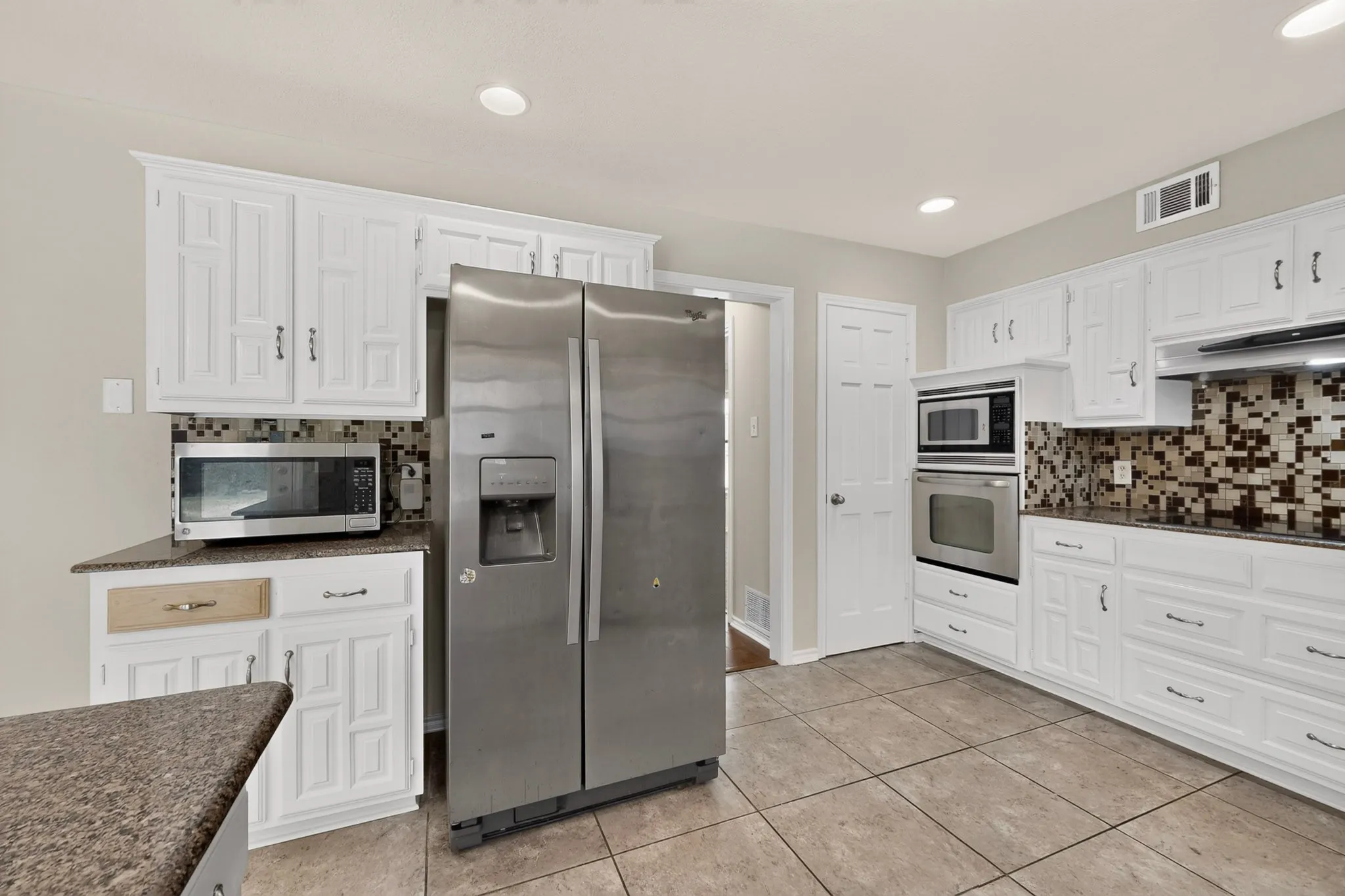 Kitchen featuring white cabinetry, stainless steel appliances, speckled countertops, and a mosaic tile backsplash