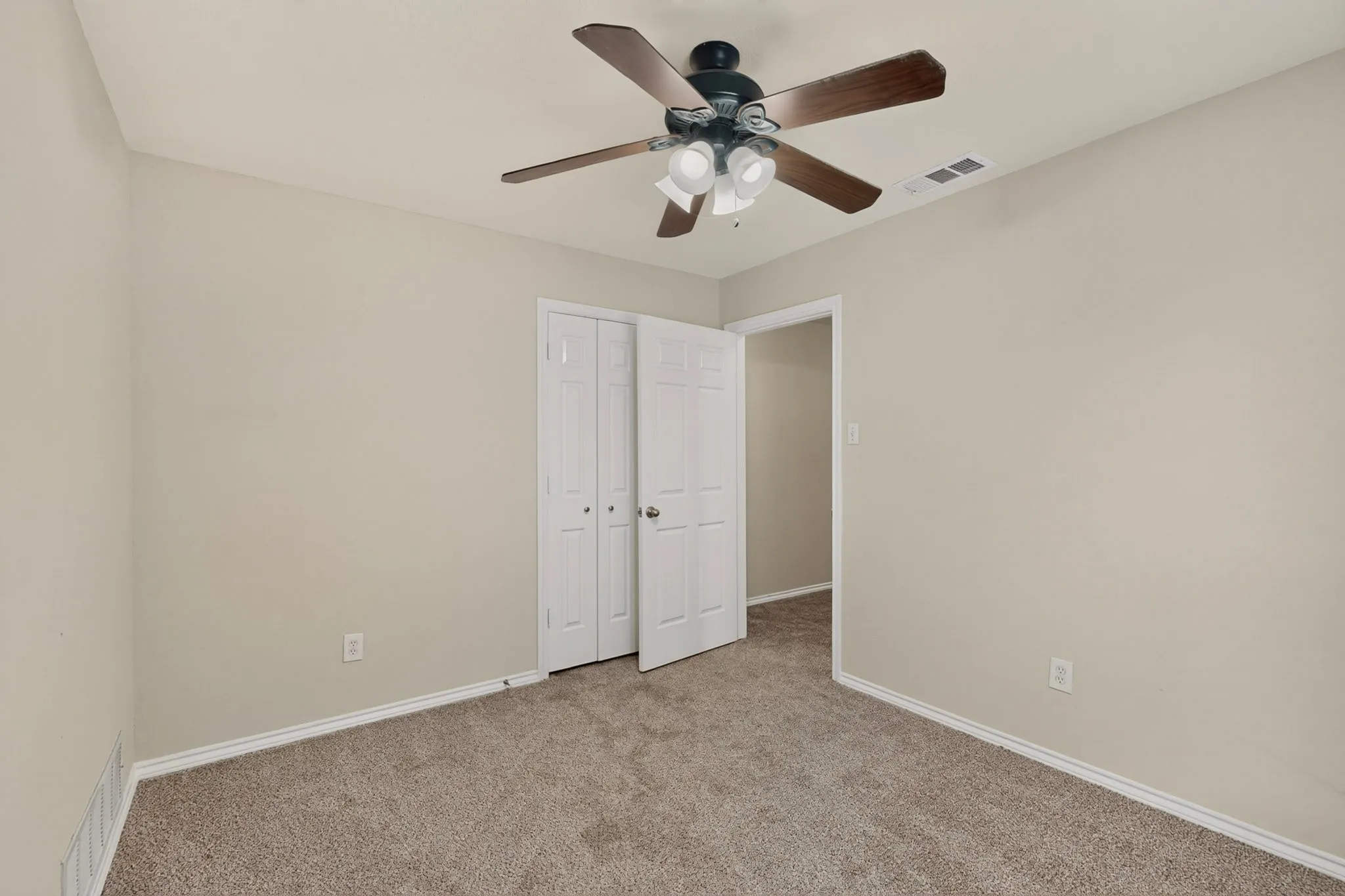 Carpeted interior space featuring a ceiling fan with integrated lighting, bi-fold closet doors, and light-toned wall paint