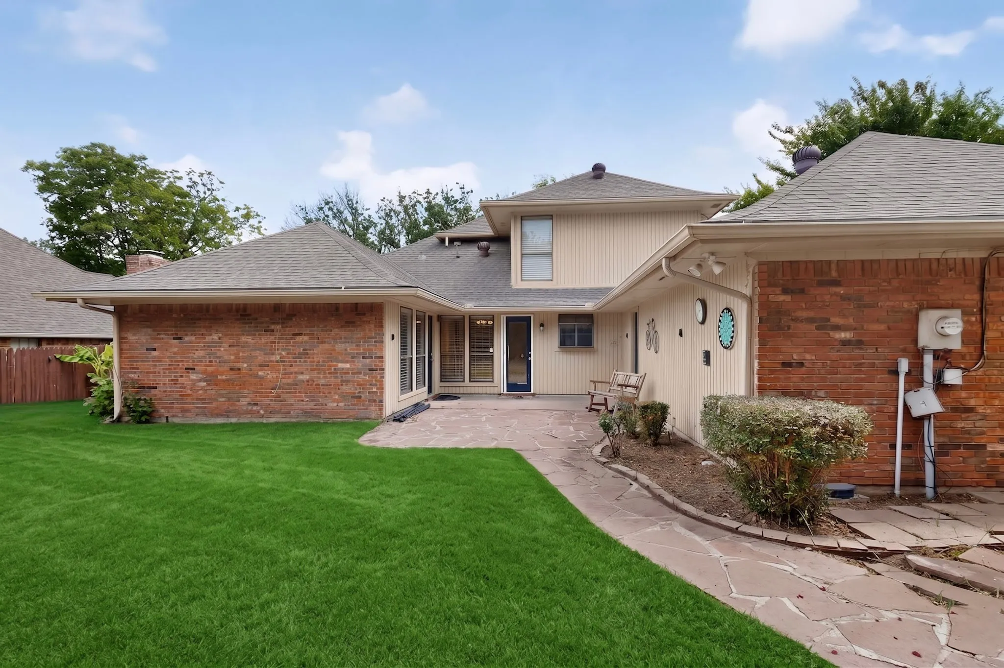 Expansive backyard featuring a stone patio, manicured lawn, and brick exterior accents