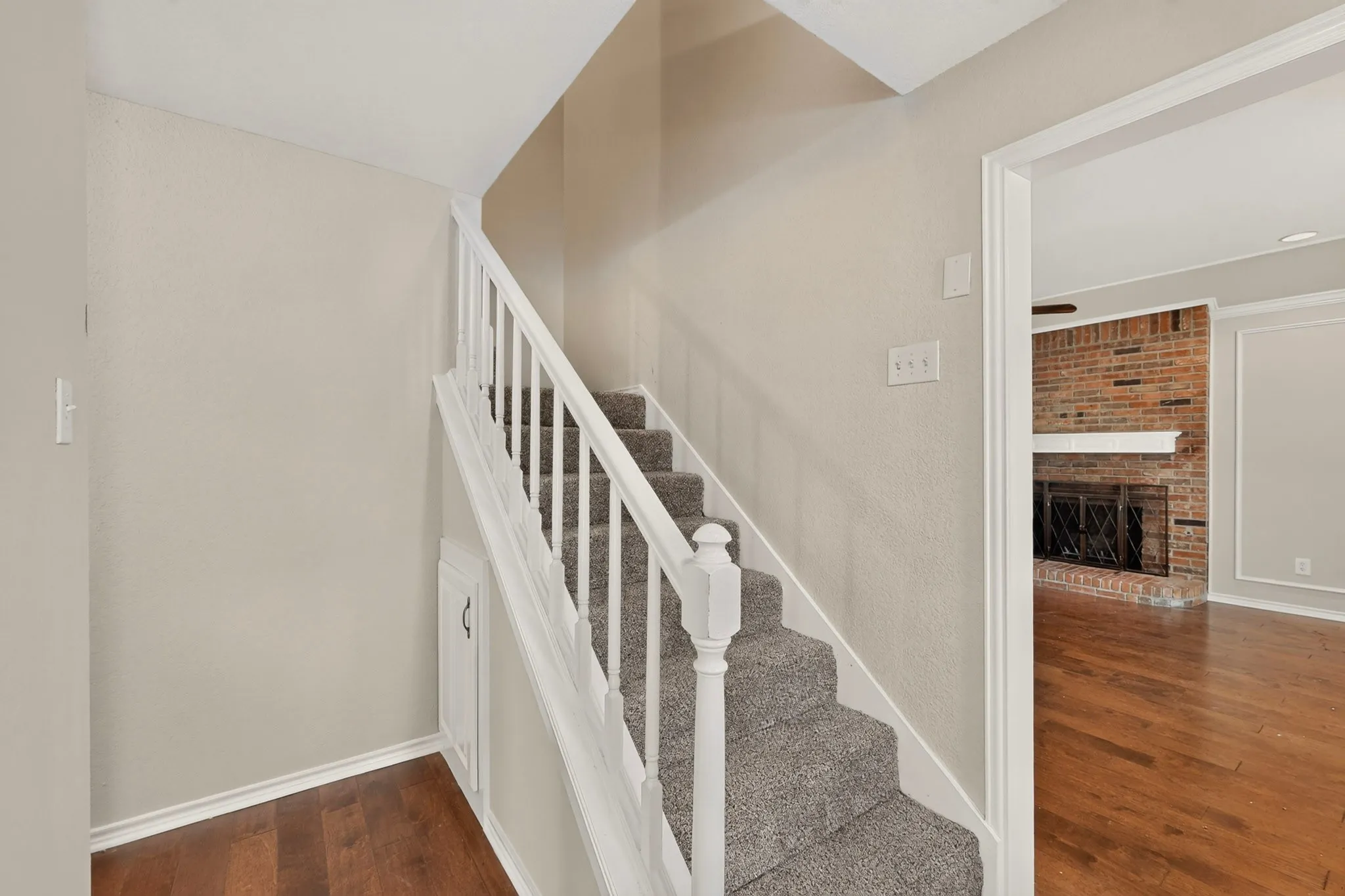Carpeted staircase with white railings, featuring hardwood flooring at the base