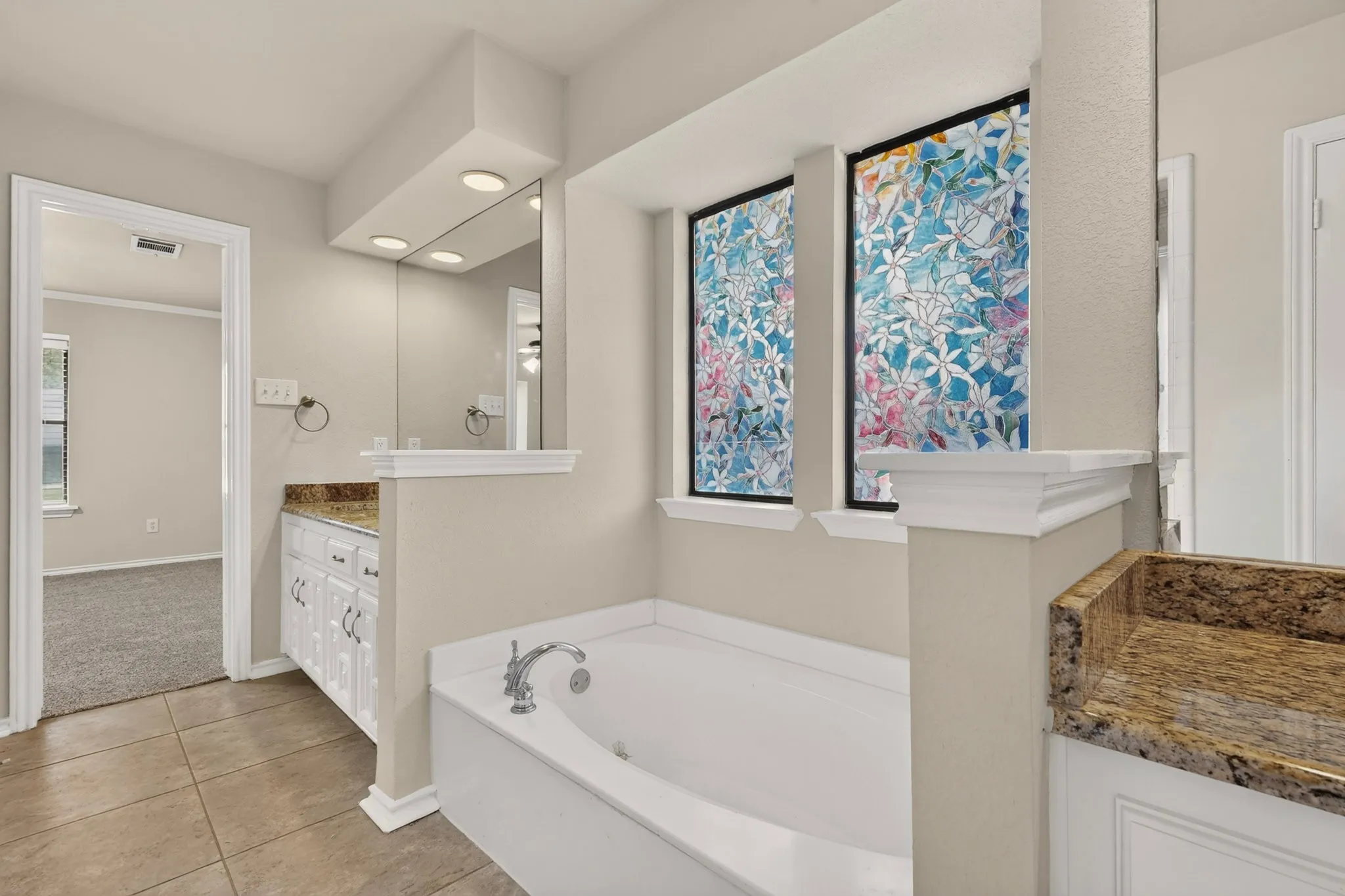 Soaking tub with chrome fixtures, framed by decorative privacy windows